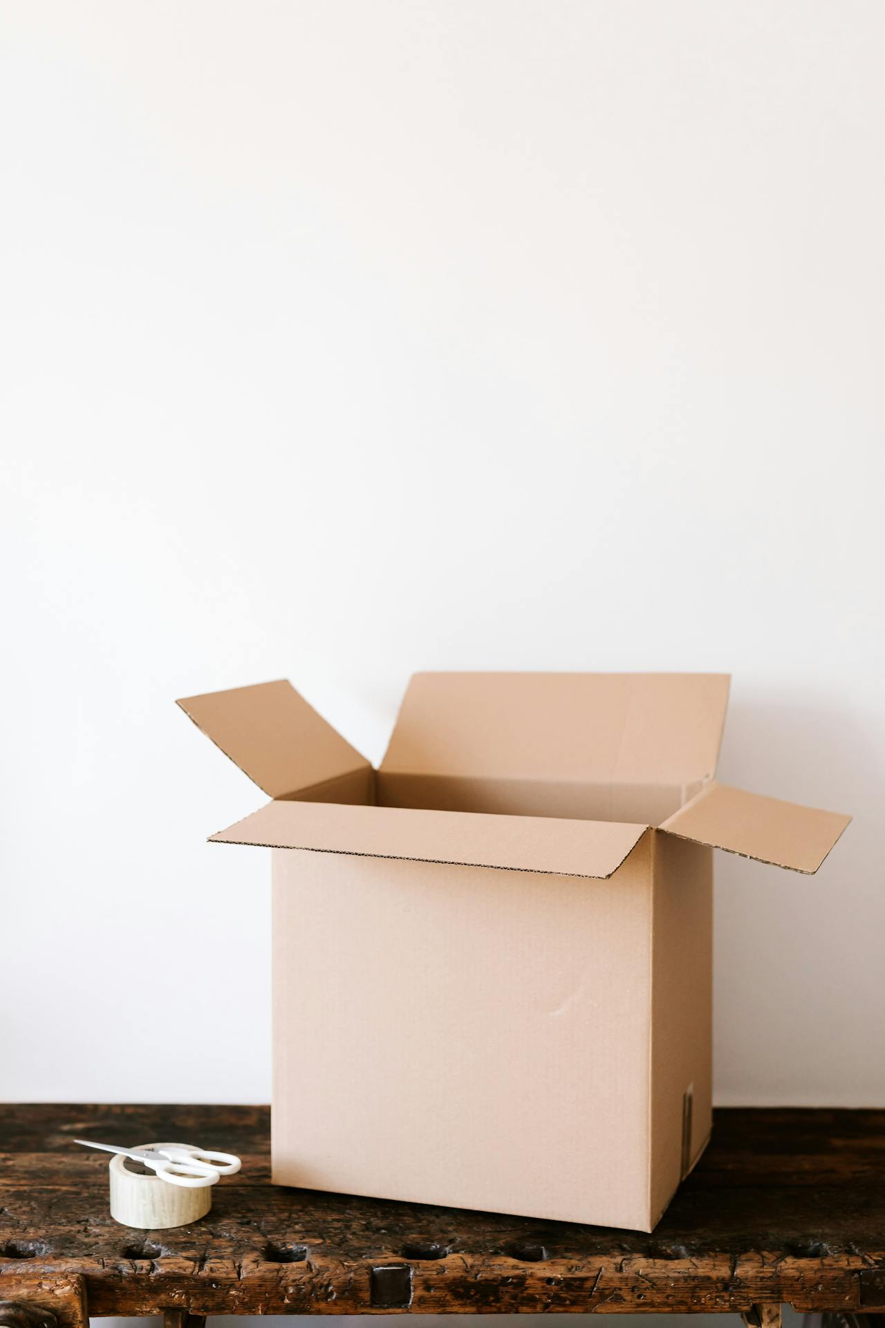 Unas tijeras, cinta adhesiva y una caja de cartón sobre una mesa | Fuente: Pexels