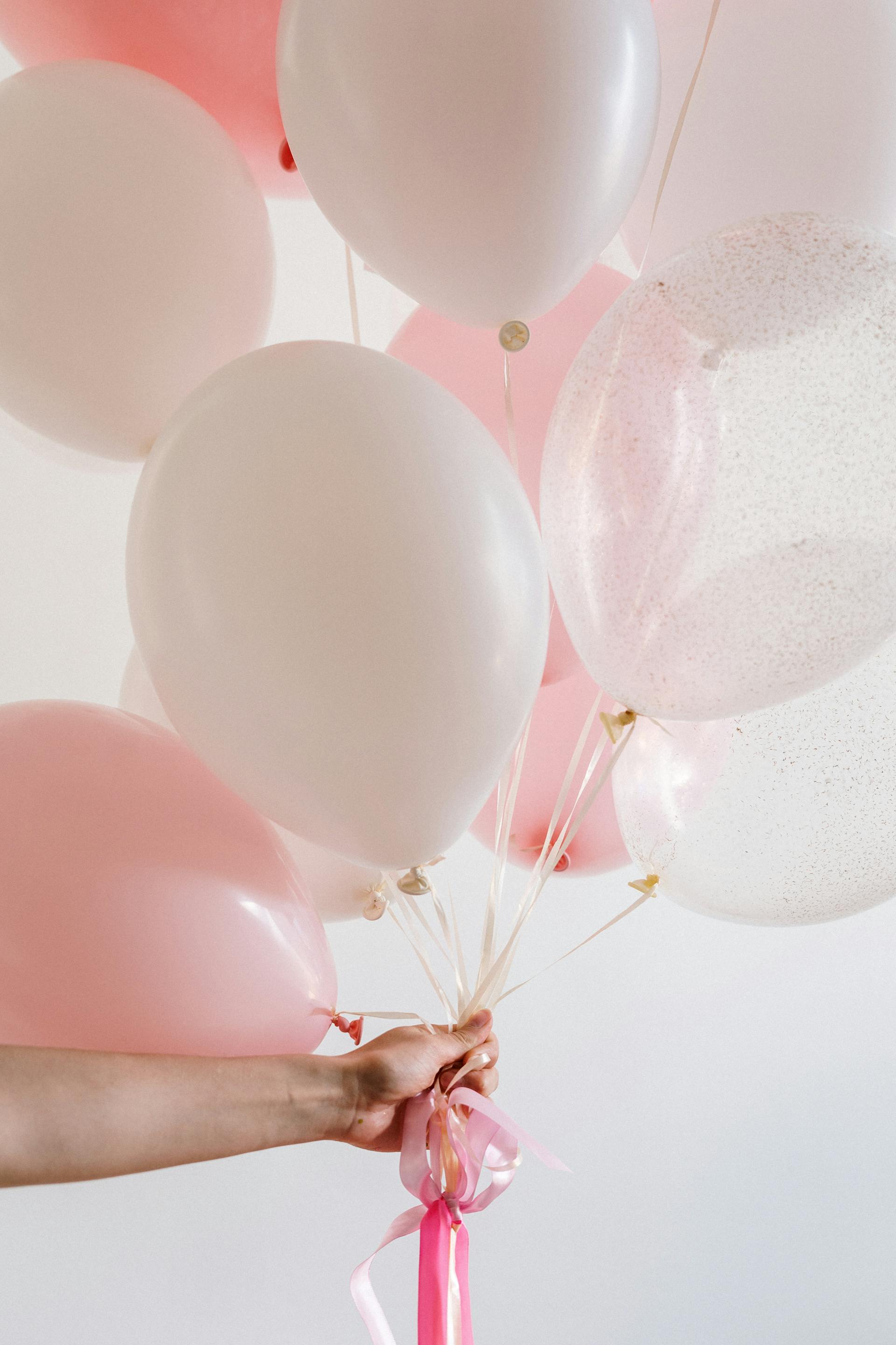 Una persona sostiene globos rosas y blancos | Fuente: Pexels