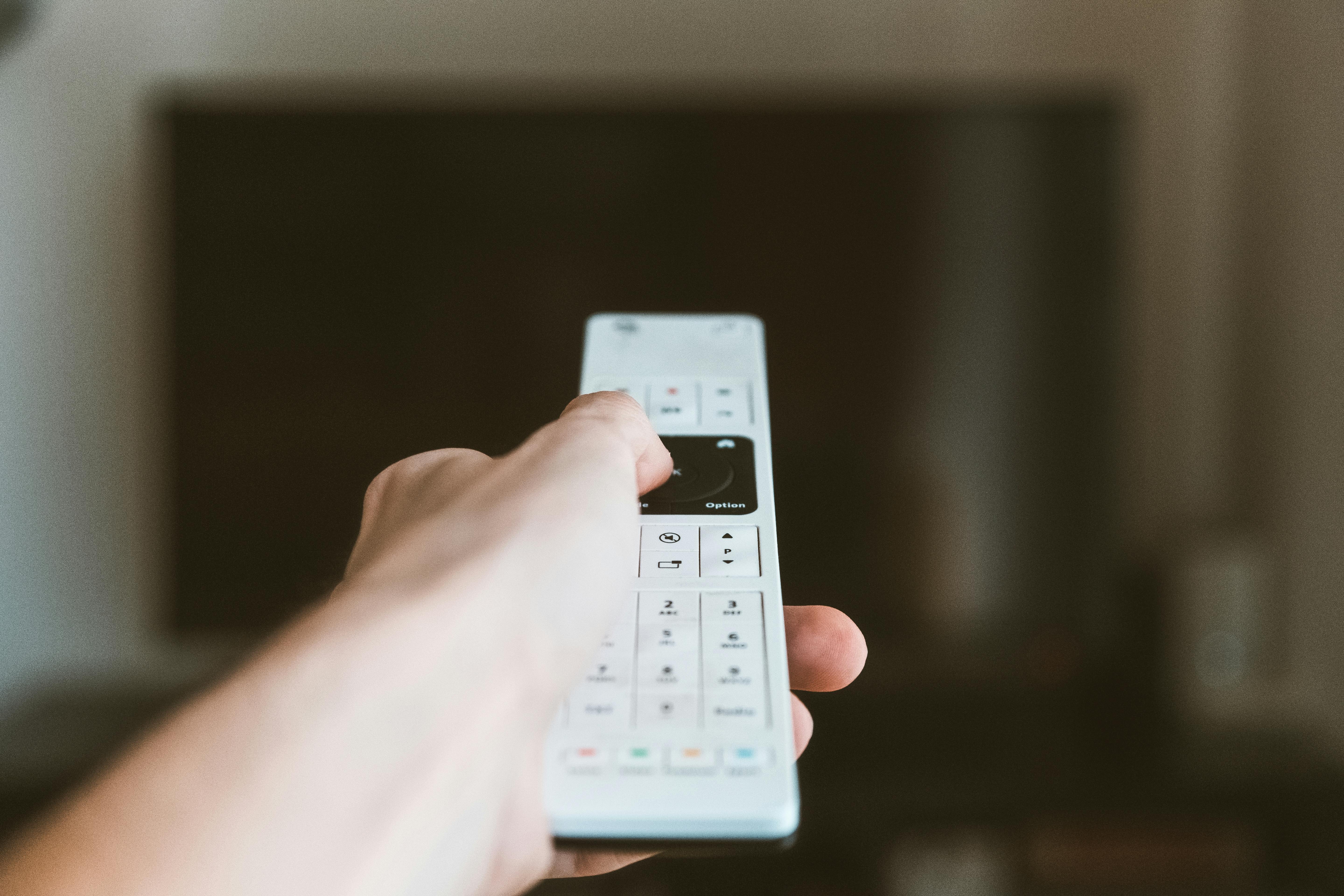 La mano de un hombre sujetando el mando a distancia de un televisor | Fuente: Pexels