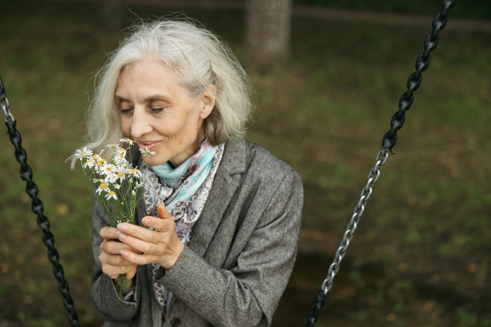 Mujer mayor sentada en un columpio y oliendo flores | Fuente: Pexels