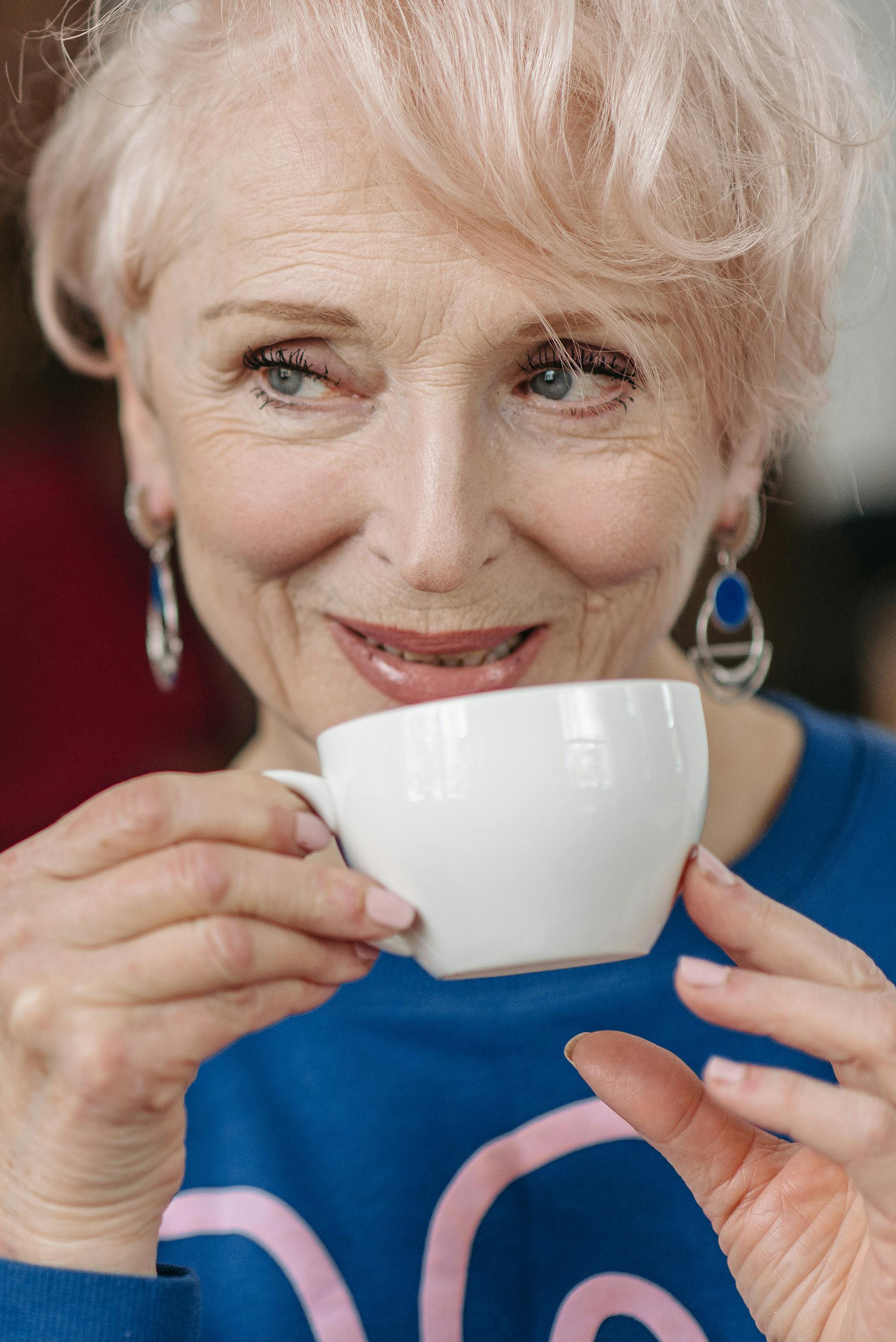 Una mujer mayor sonriente bebiendo su café mientras mira a alguien | Fuente: Pexels