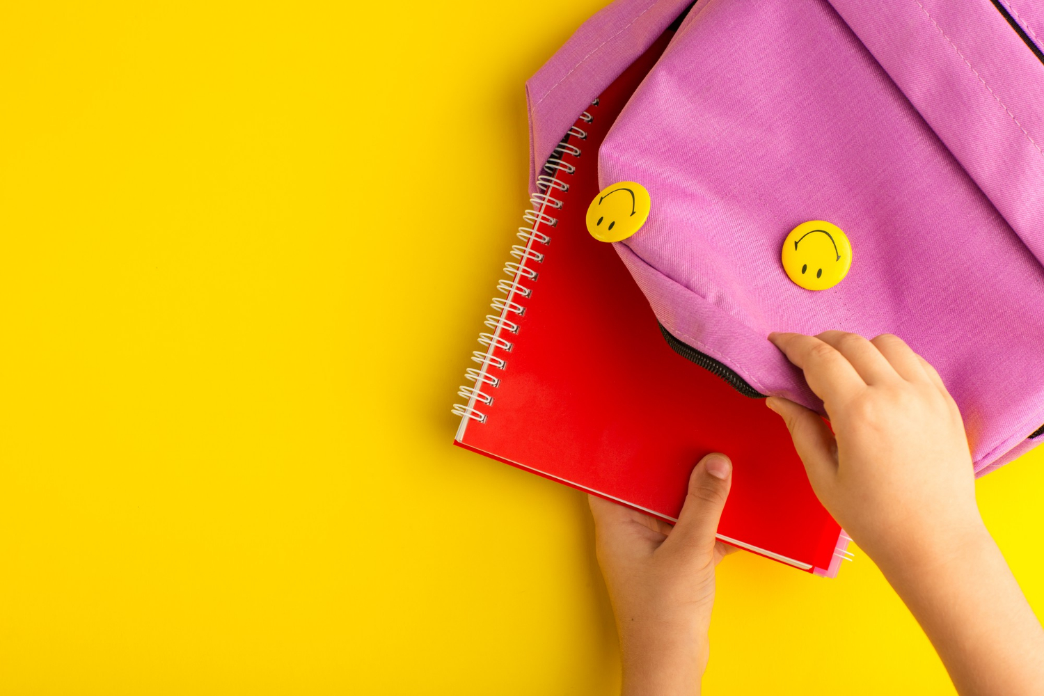 Primer plano de un niño metiendo un cuaderno en una bolsa rosa | Fuente: Freepik