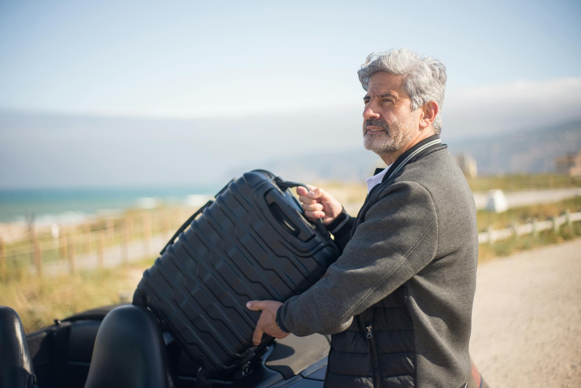 Un hombre con chaqueta gris sujetando una maleta | Fuente: Pexels