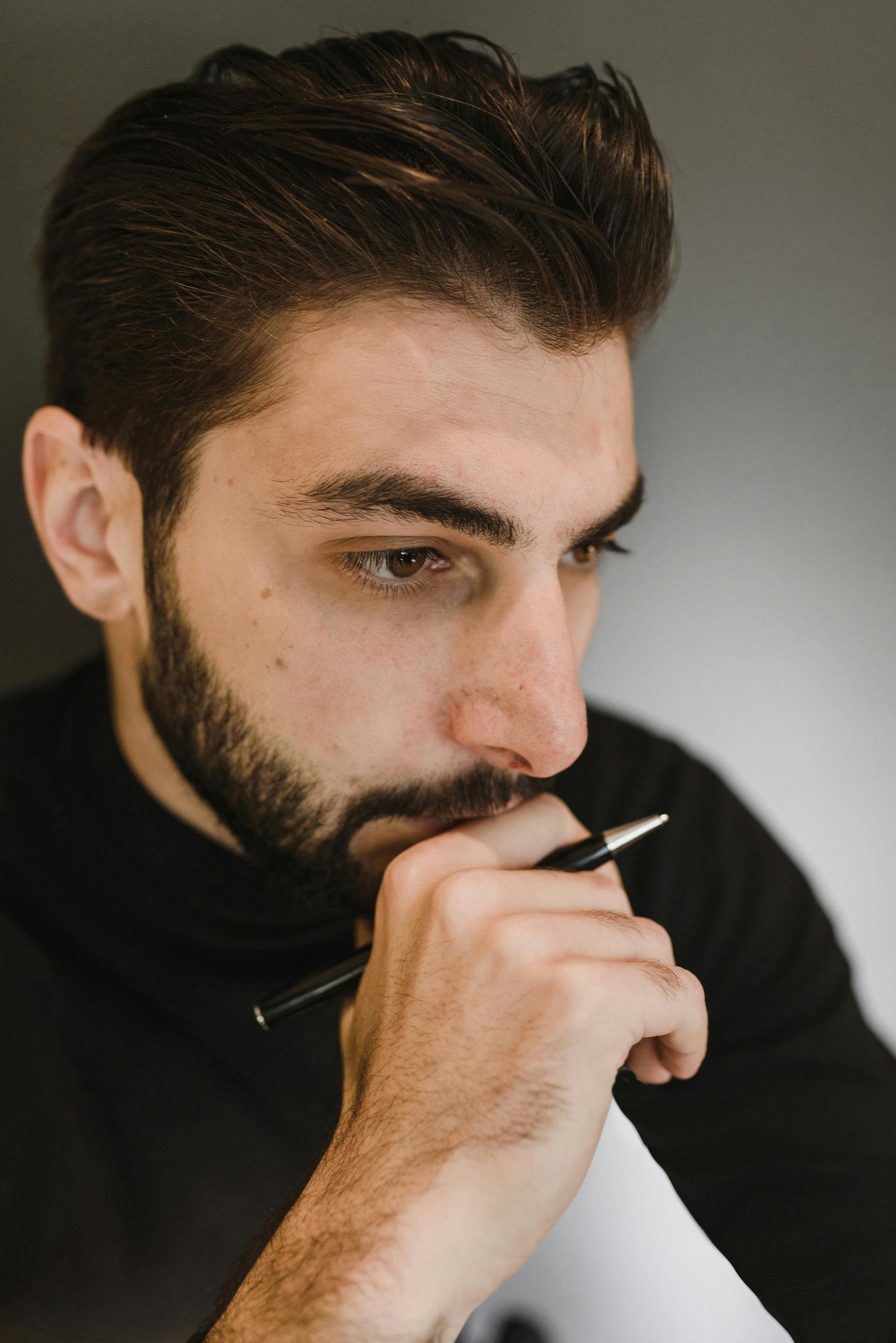 Hombre sujetando un bolígrafo mientras piensa | Fuente: Pexels