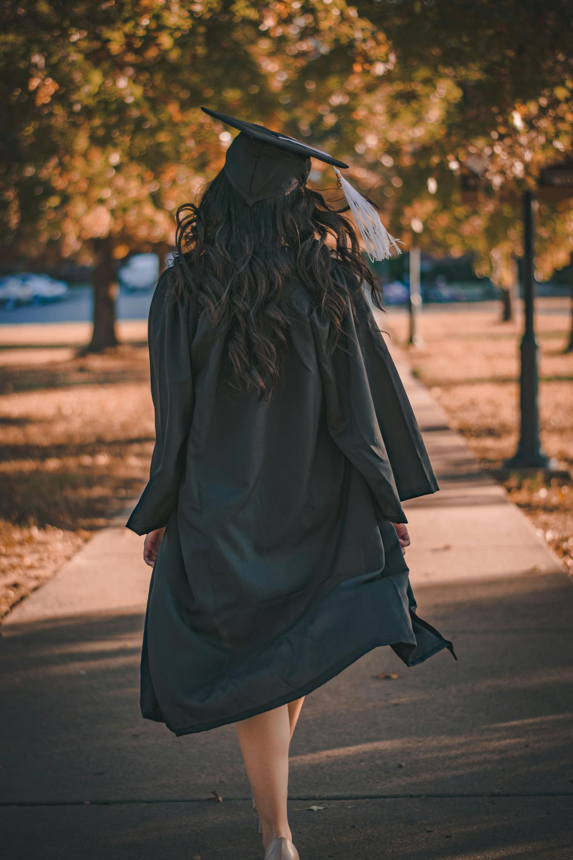 Una mujer con toga y birrete caminando por un sendero | Fuente: Pexels