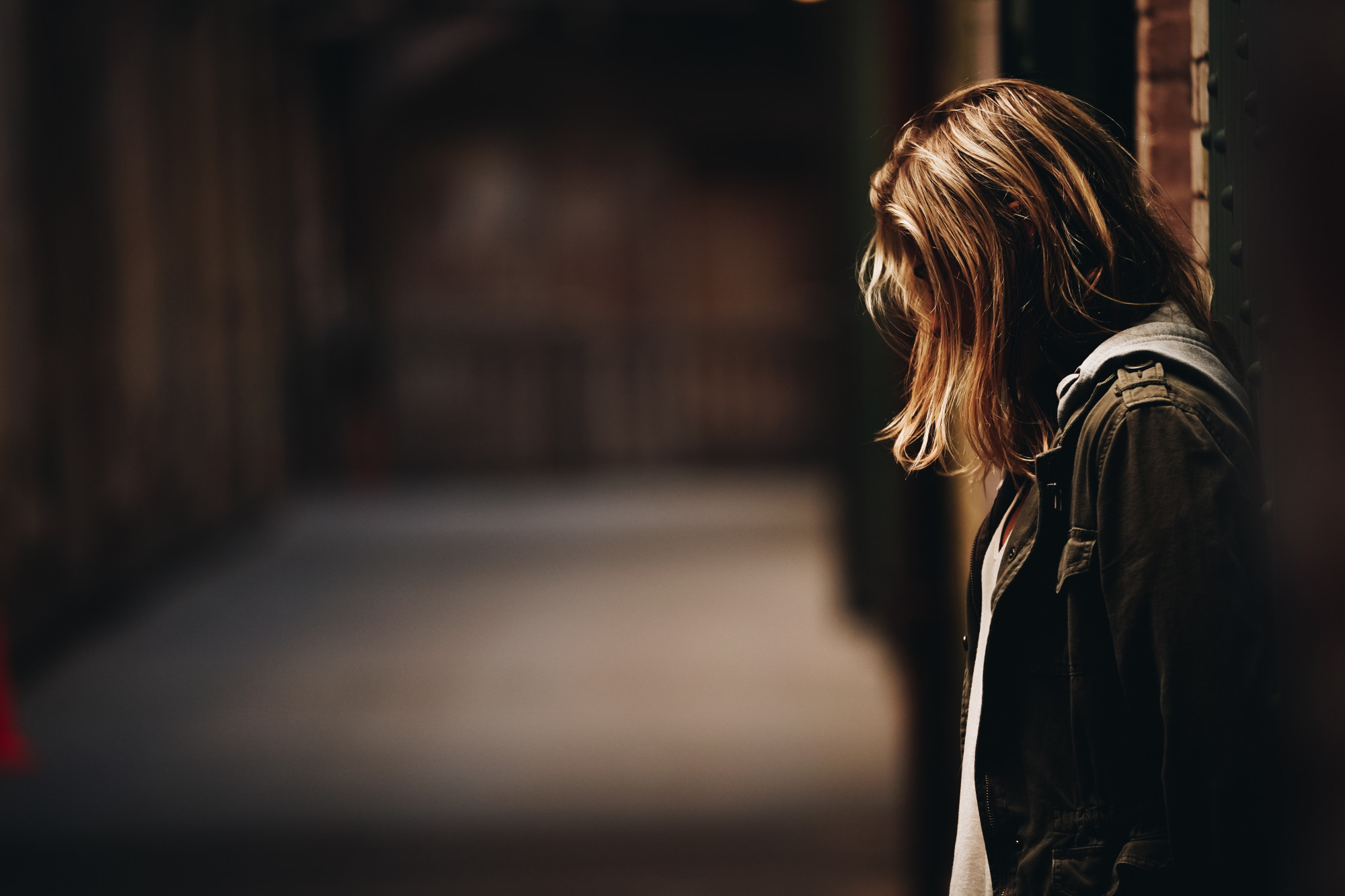 Una adolescente apoyada en la pared, mirando hacia abajo en un pasillo | Fuente: Freepik