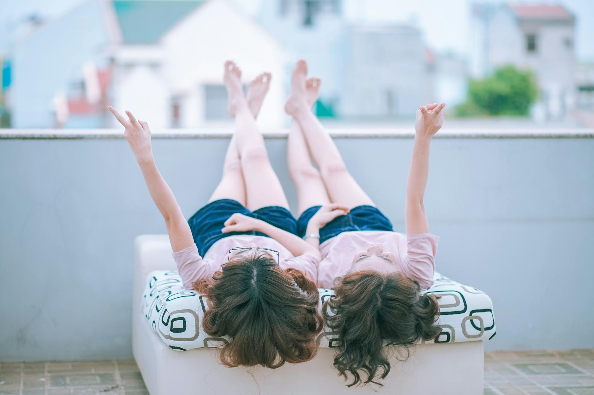 Dos mujeres jóvenes tumbadas en un balcón y mostrando signos de paz | Fuente: Pexels