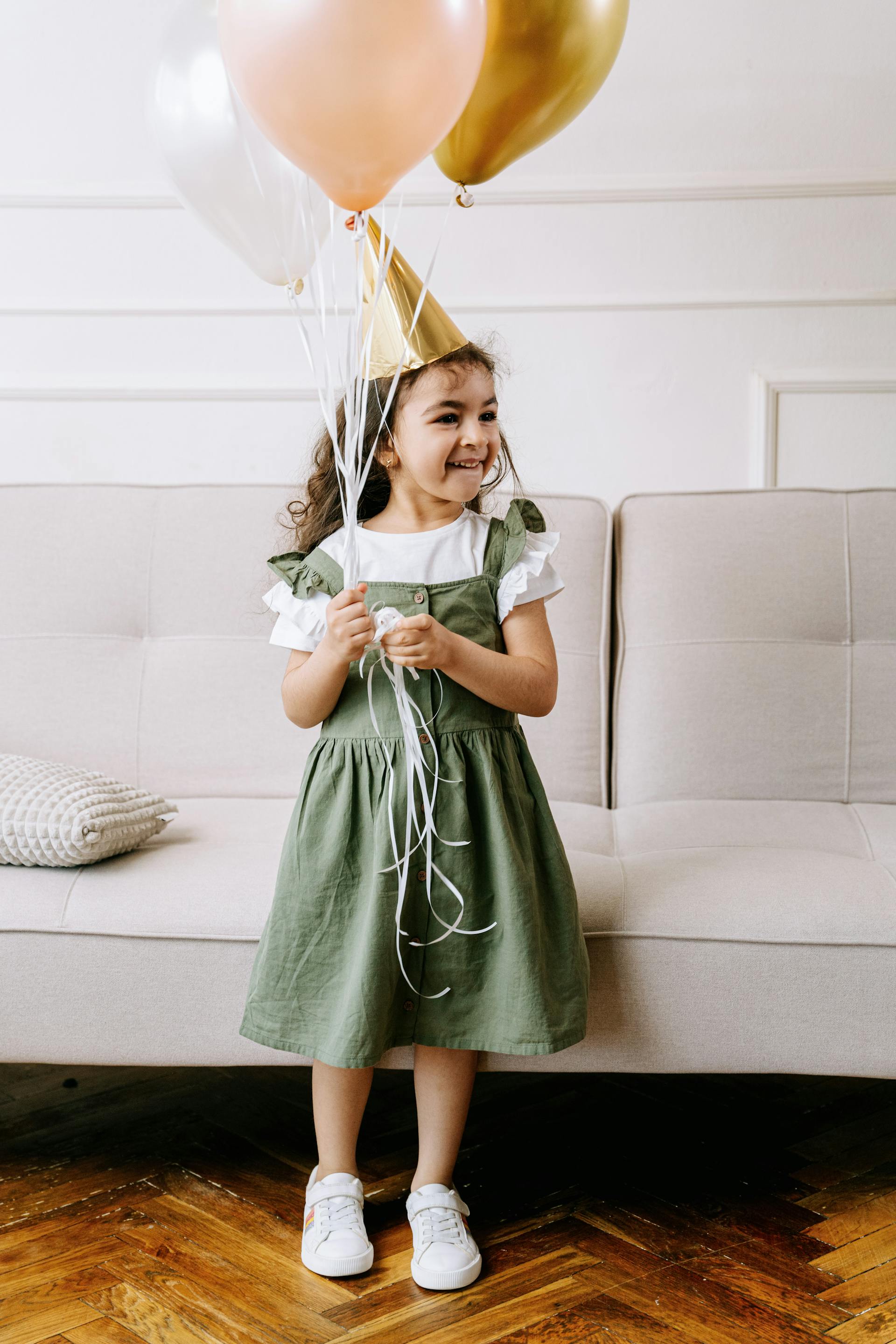 Una niña con un sombrero de fiesta mientras sostiene globos | Fuente: Pexels