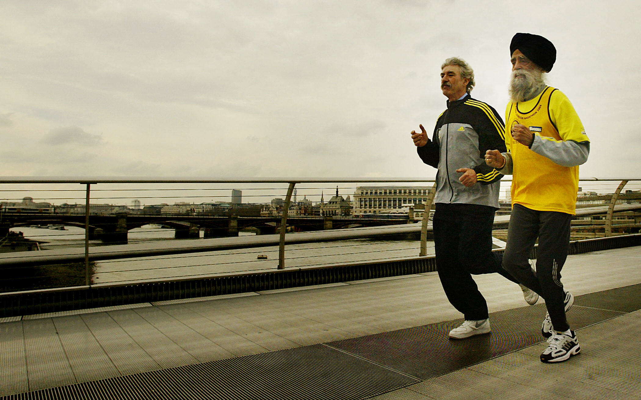 Fauja Singh y el director de la carrera David Bedford corriendo por el Puente del Milenio tras el Maratón Flora de Londres el 1 de abril de 2004. | Fuente: Getty Images