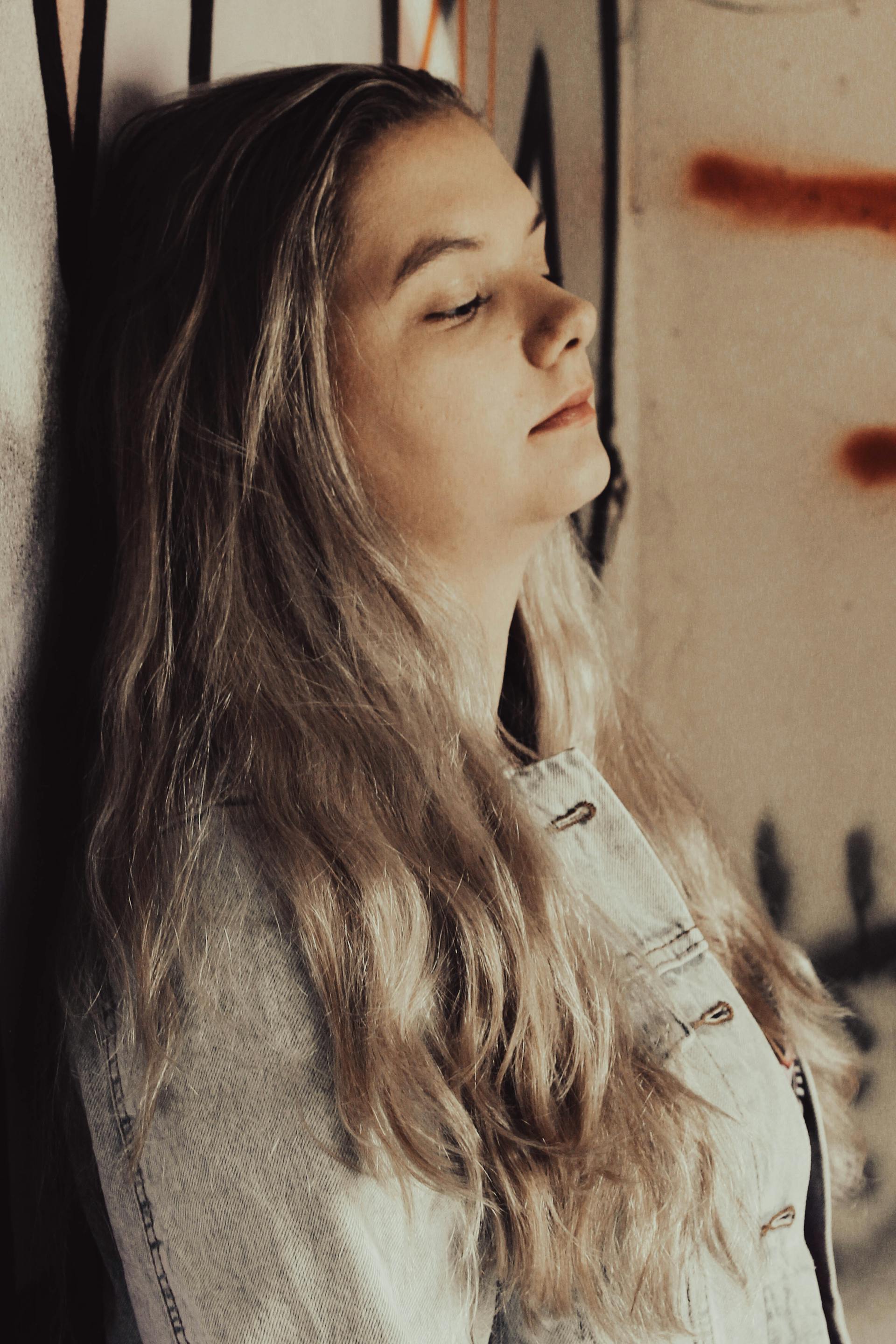 Una mujer triste con una chaqueta vaquera y los ojos cerrados, apoyada en una pared | Fuente: Pexels