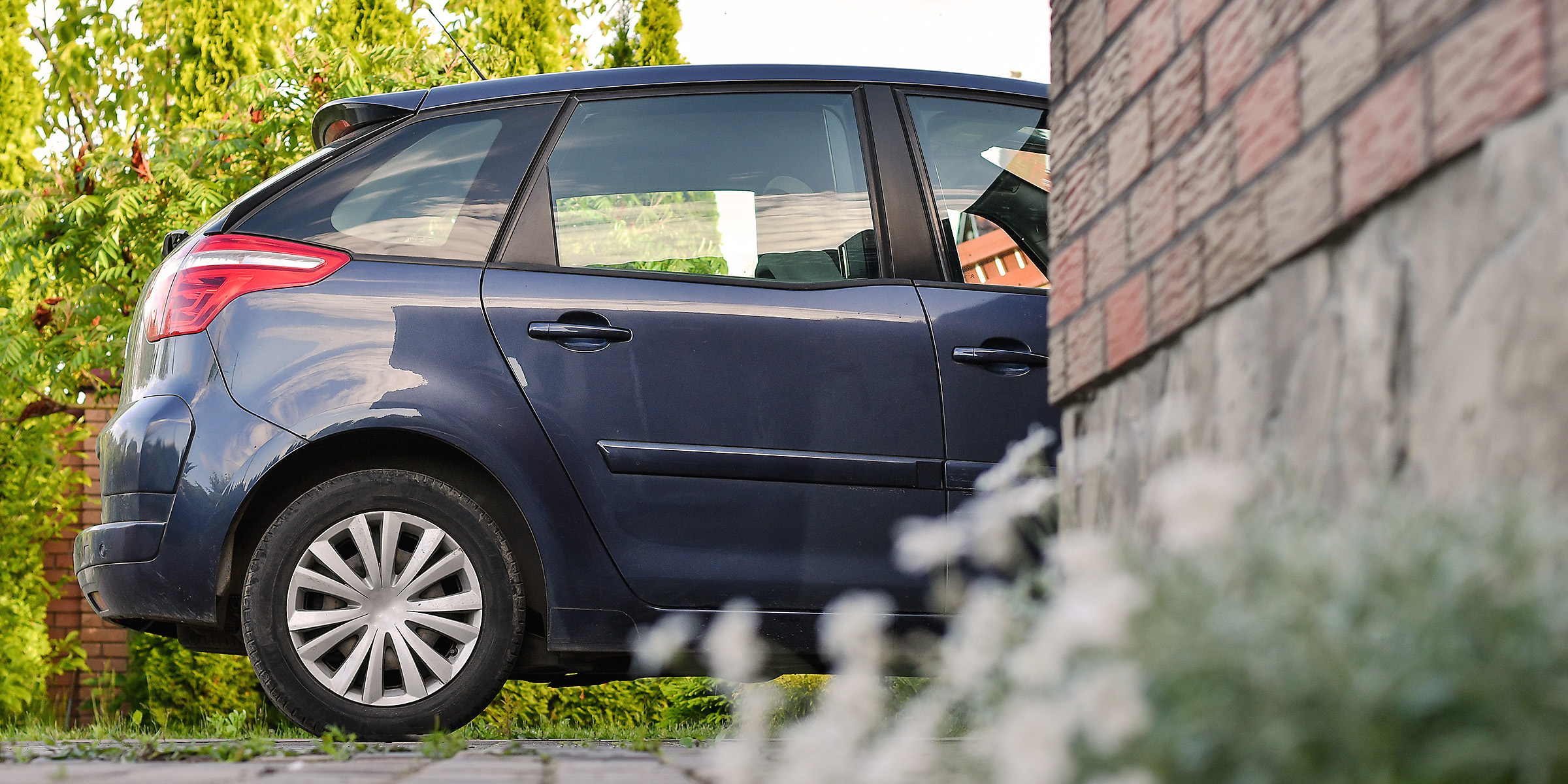 Un Automóvil azul oscuro aparcado junto a un muro de ladrillo en un barrio tranquilo | Fuente: Shutterstock