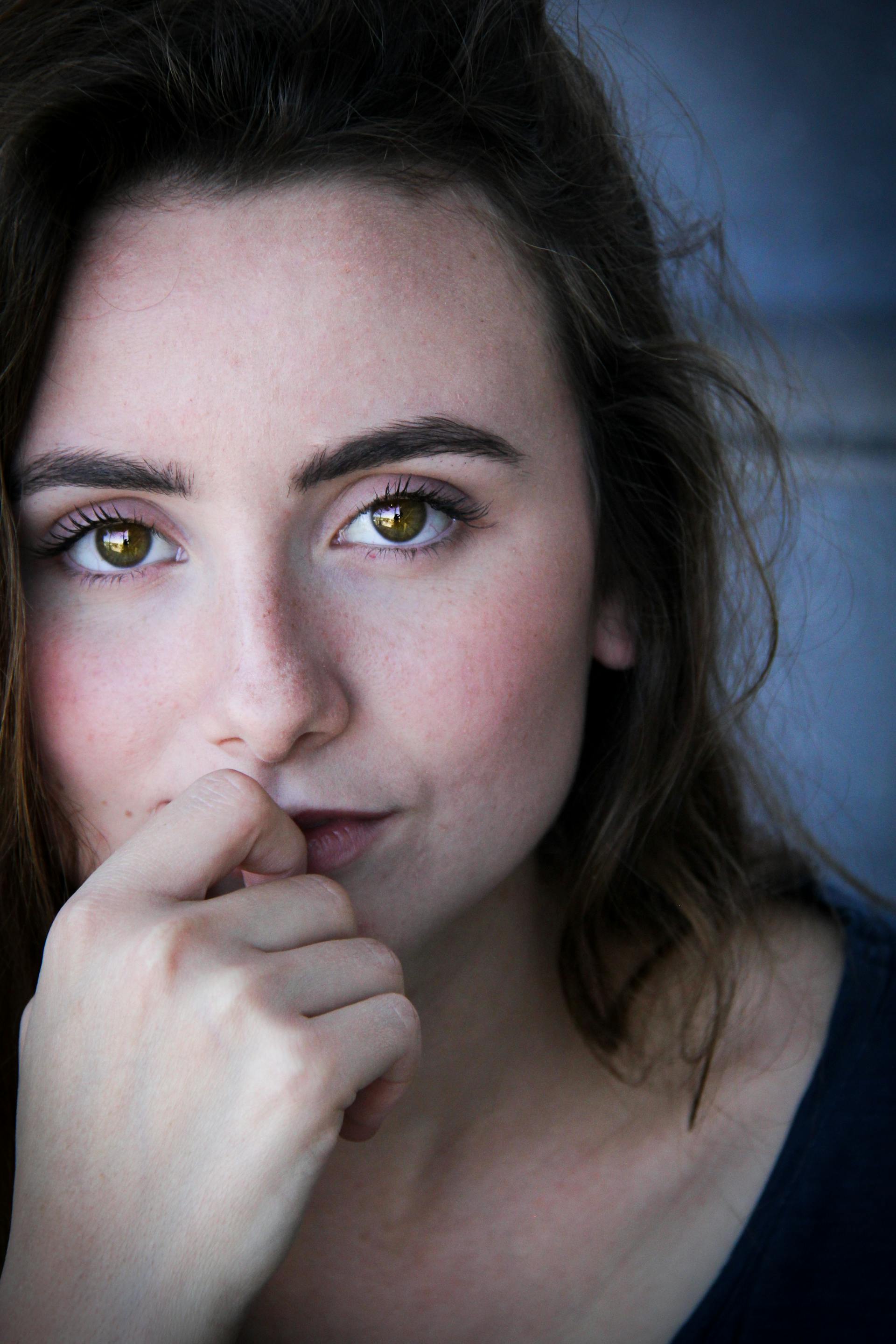 Una mujer de pelo castaño y ojos verdes llevándose el dedo a los labios | Fuente: Pexels