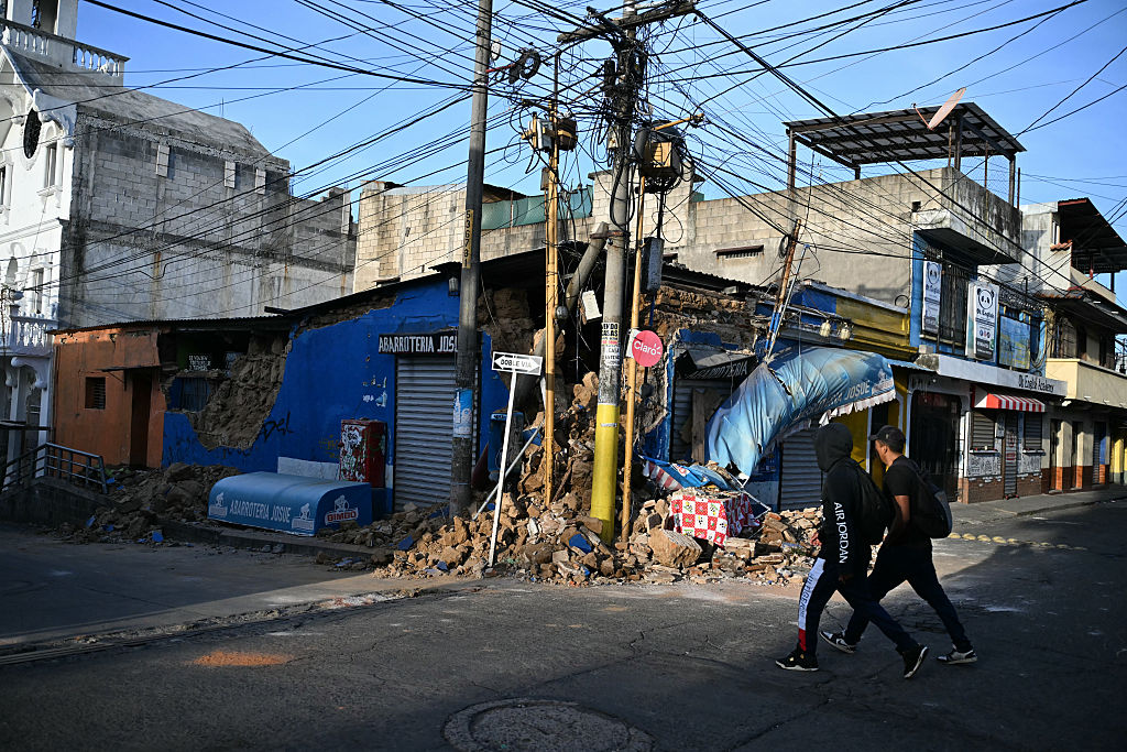Hombres pasan junto al muro derrumbado de una tienda tras una serie de sismos que sacudieron la zona en Palin, Guatemala, el 9 de julio de 2025. | Foto: Getty Images