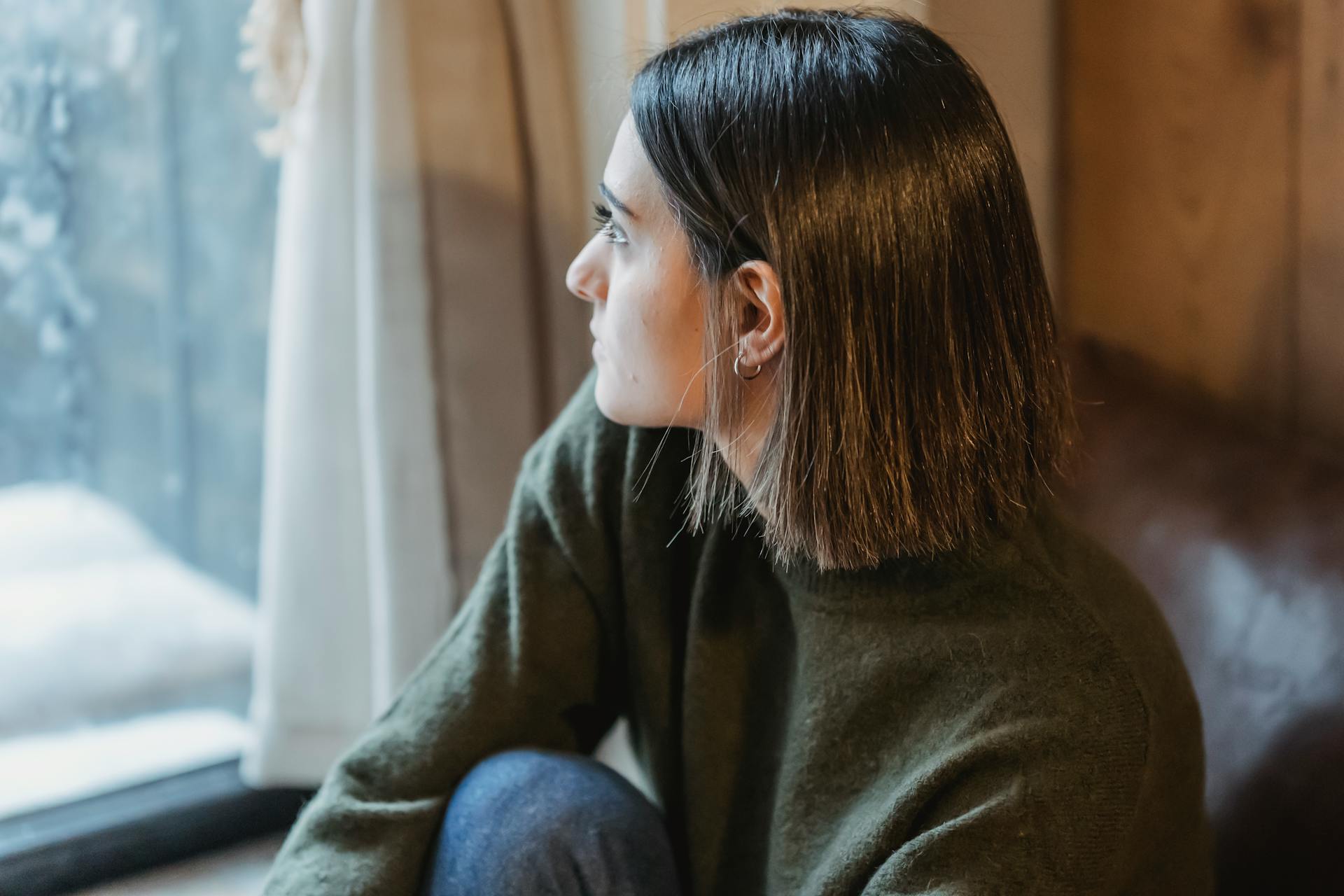 Una mujer pensativa sentada junto a la ventana | Fuente: Pexels