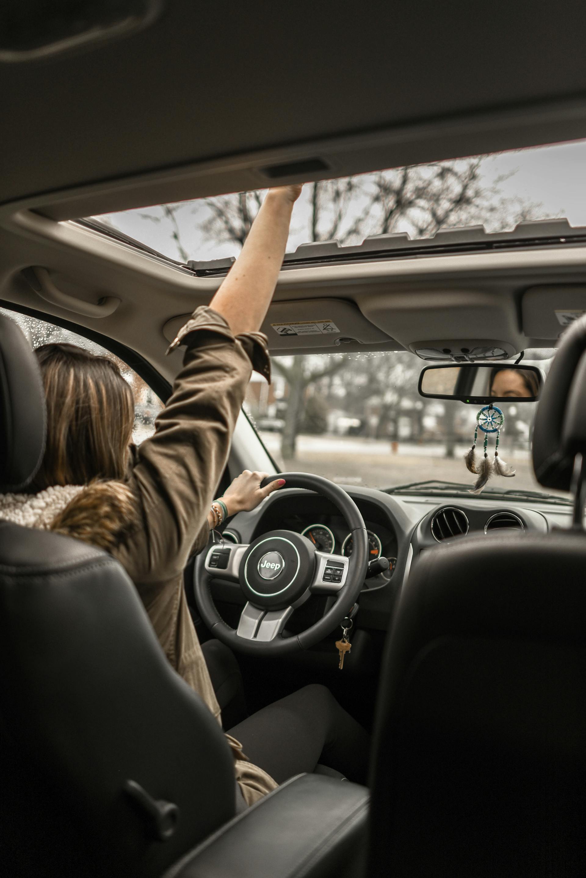 Una mujer saluda a través de un techo solar abierto en un auto | Fuente: Pexels