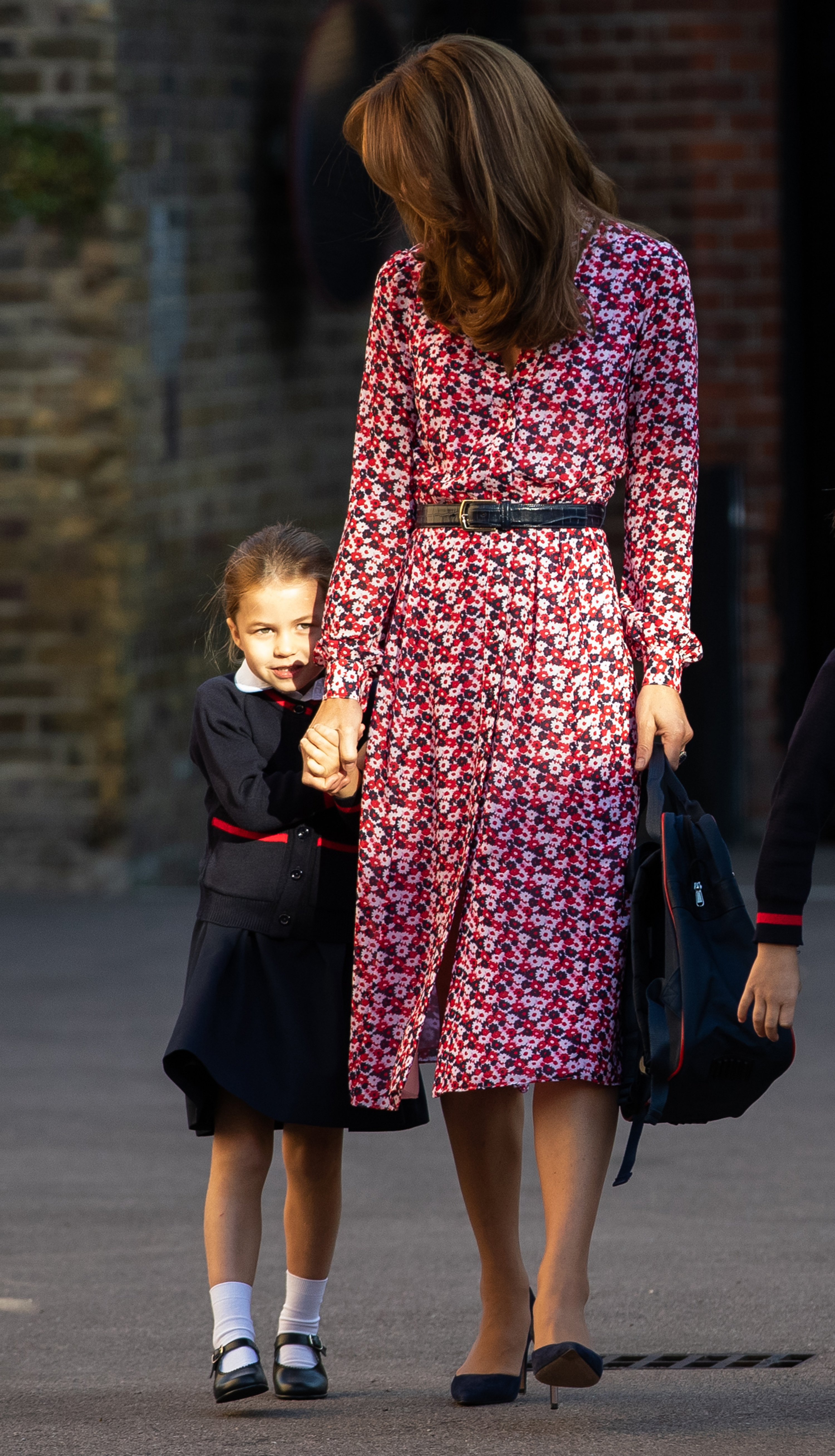 La princesa Charlotte va de la mano de su madre, Catherine, al llegar a su primer día de colegio en Thomas’s Battersea el 5 de septiembre de 2019, en Londres, Inglaterra. La pequeña de la realeza mira tímidamente a los curiosos con su uniforme escolar, compuesto por una falda azul marino y roja, un cárdigan, calcetines blancos hasta el tobillo y zapatos negros tipo Mary Jane, acompañada por la duquesa, que lleva un vestido midi floral rosa y azul marino con cinturón y unos zapatos de salón azul marino de punta. | Fuente: Getty Images