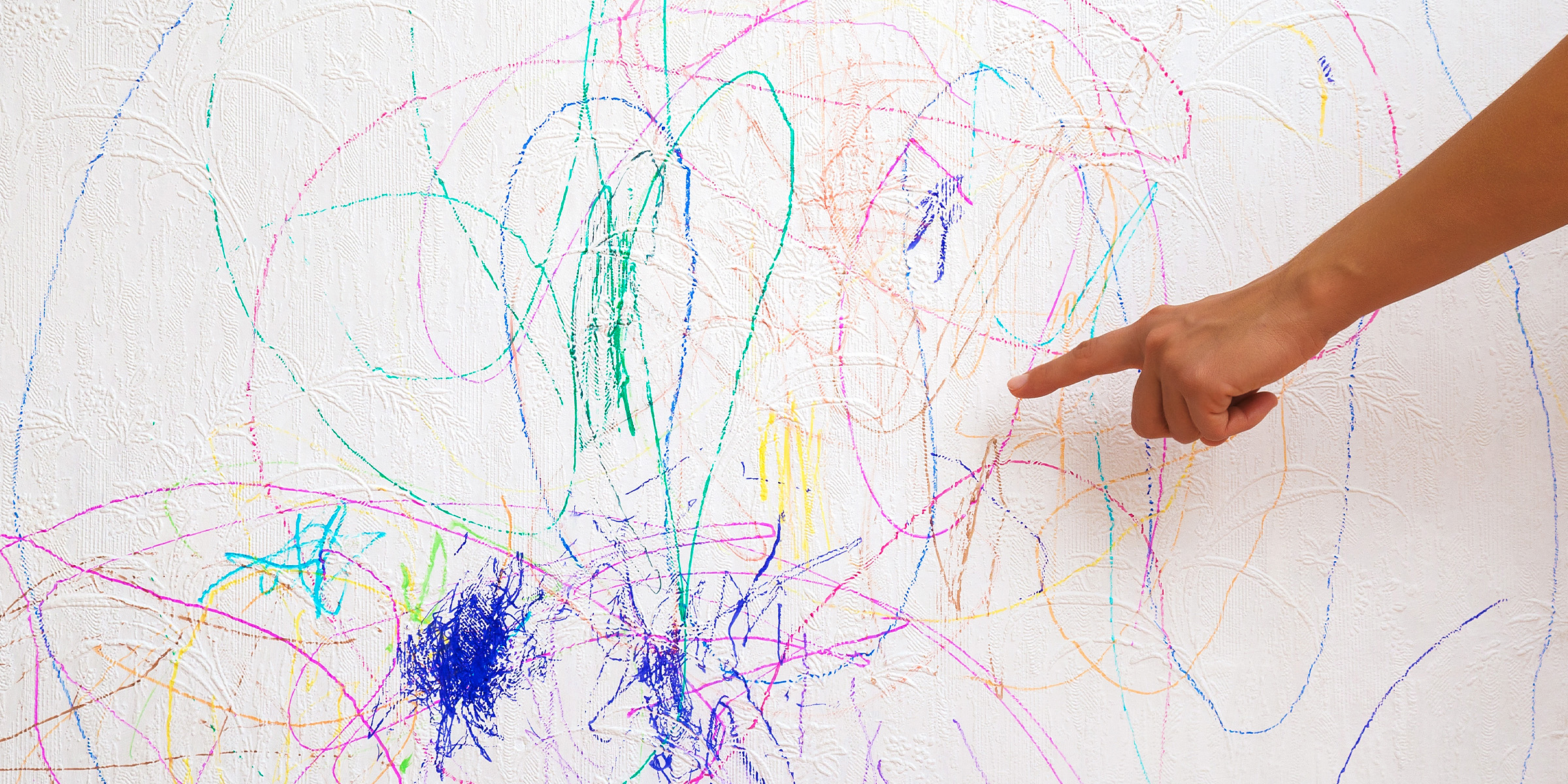 Un dedo señalando arañazos de colores en una pared | Fuente: Shutterstock