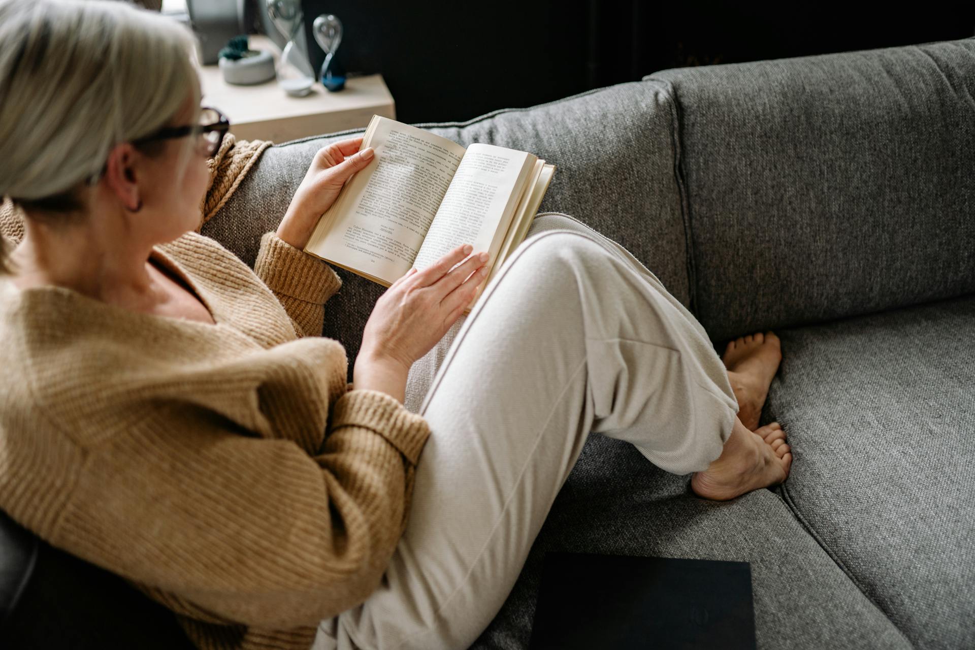 Una mujer mayor leyendo un libro sentada en un sofá | Fuente: Pexels