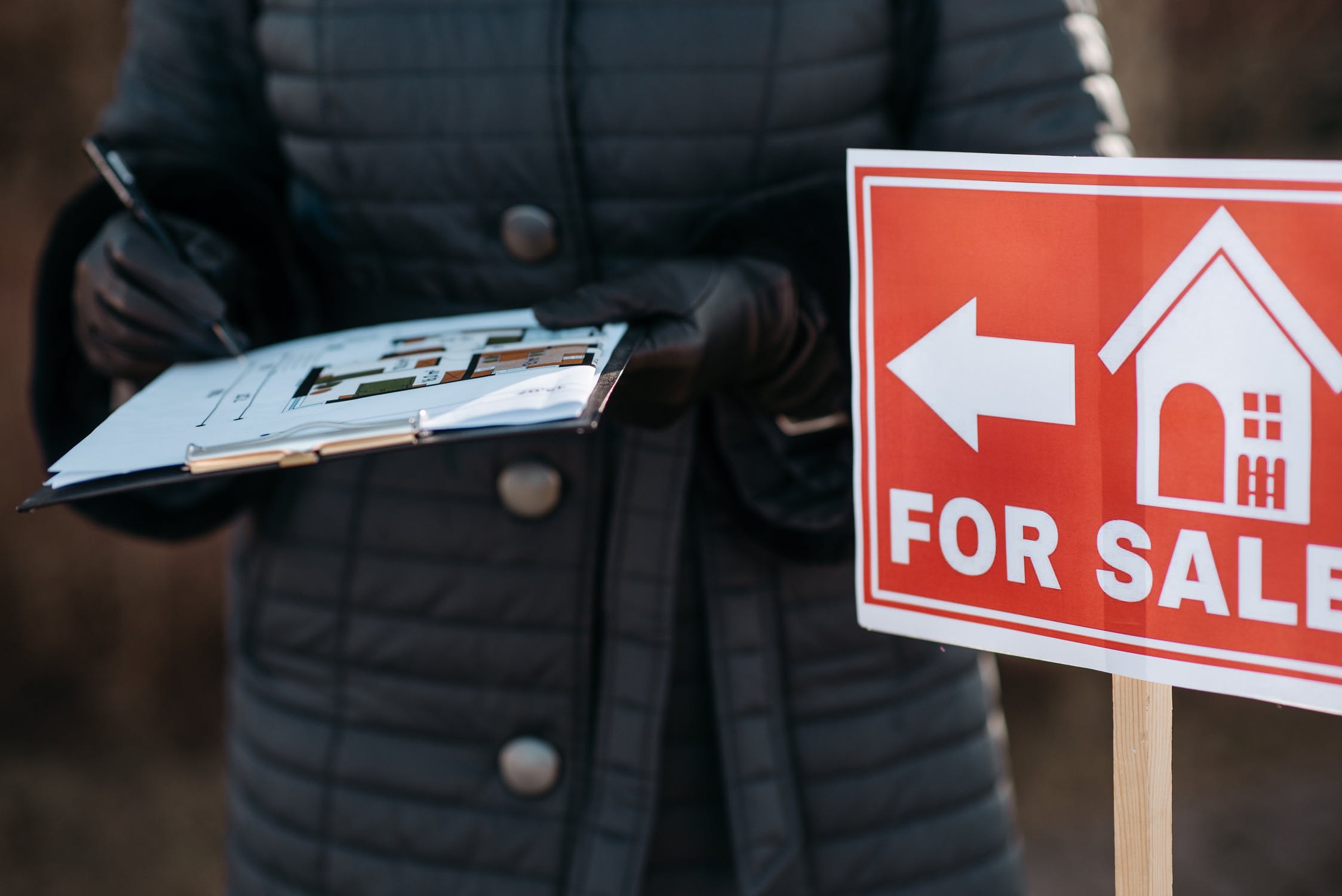 Un hombre firmando unos papeles junto a un carte de "Se Vende" | Fuente: Pexels