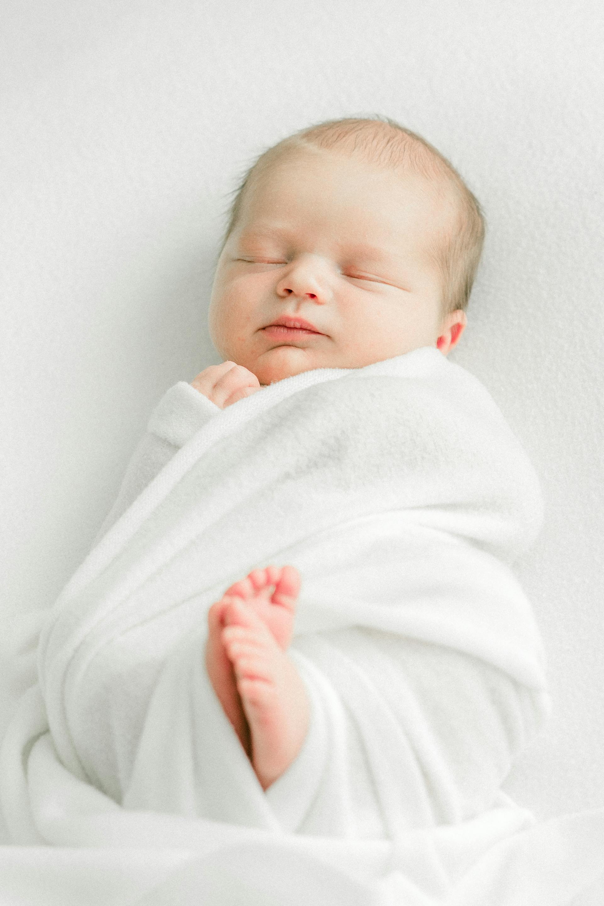 Un bebé recién nacido durmiendo envuelto en una manta blanca | Fuente: Pexels