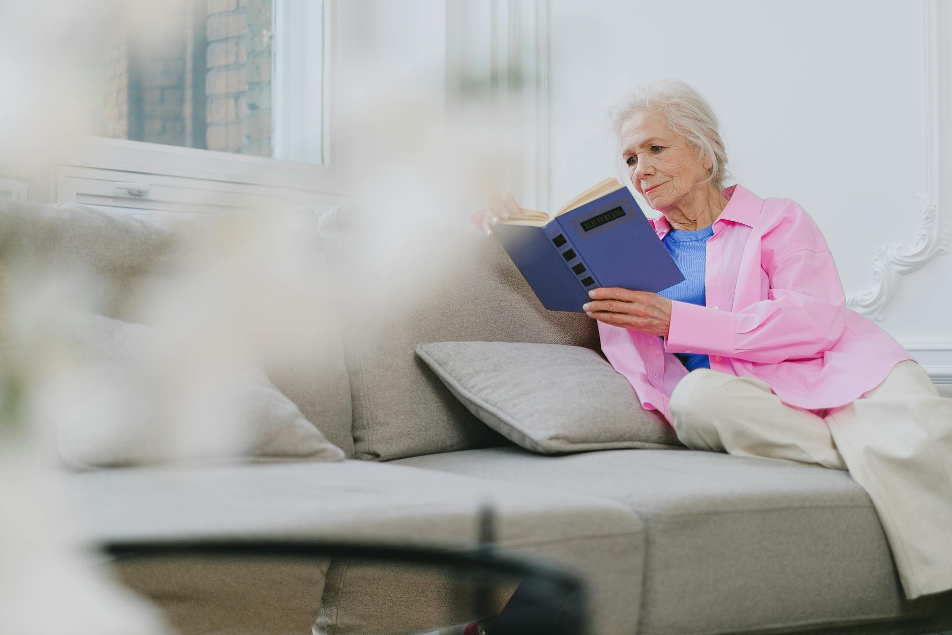 Una anciana sentada en el sofá y leyendo un libro | Fuente: Pexels