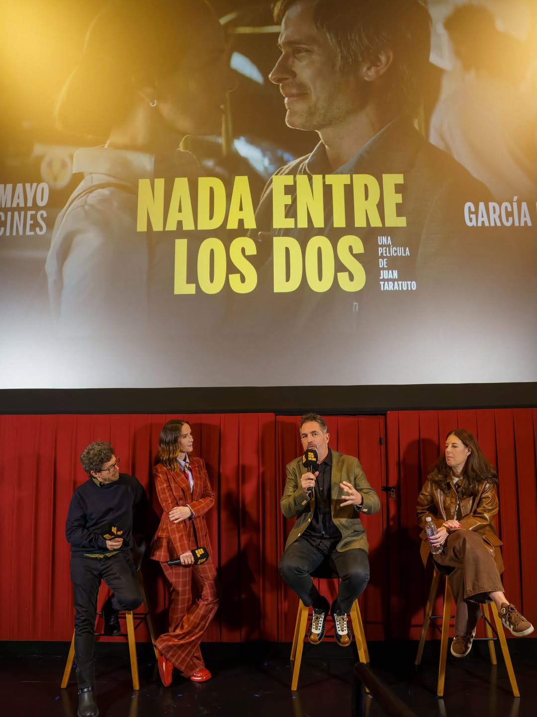 Natalia Oreiro participa en la presentación de “Nada entre los dos” junto a Juan Taratuto y otros integrantes del elenco. La actriz luce su conjunto sastrero de cuadros rojizos mientras el director habla con un micrófono frente a la pantalla con el afiche de la película. | Fuente: Instagram/nataliaoreirosoy