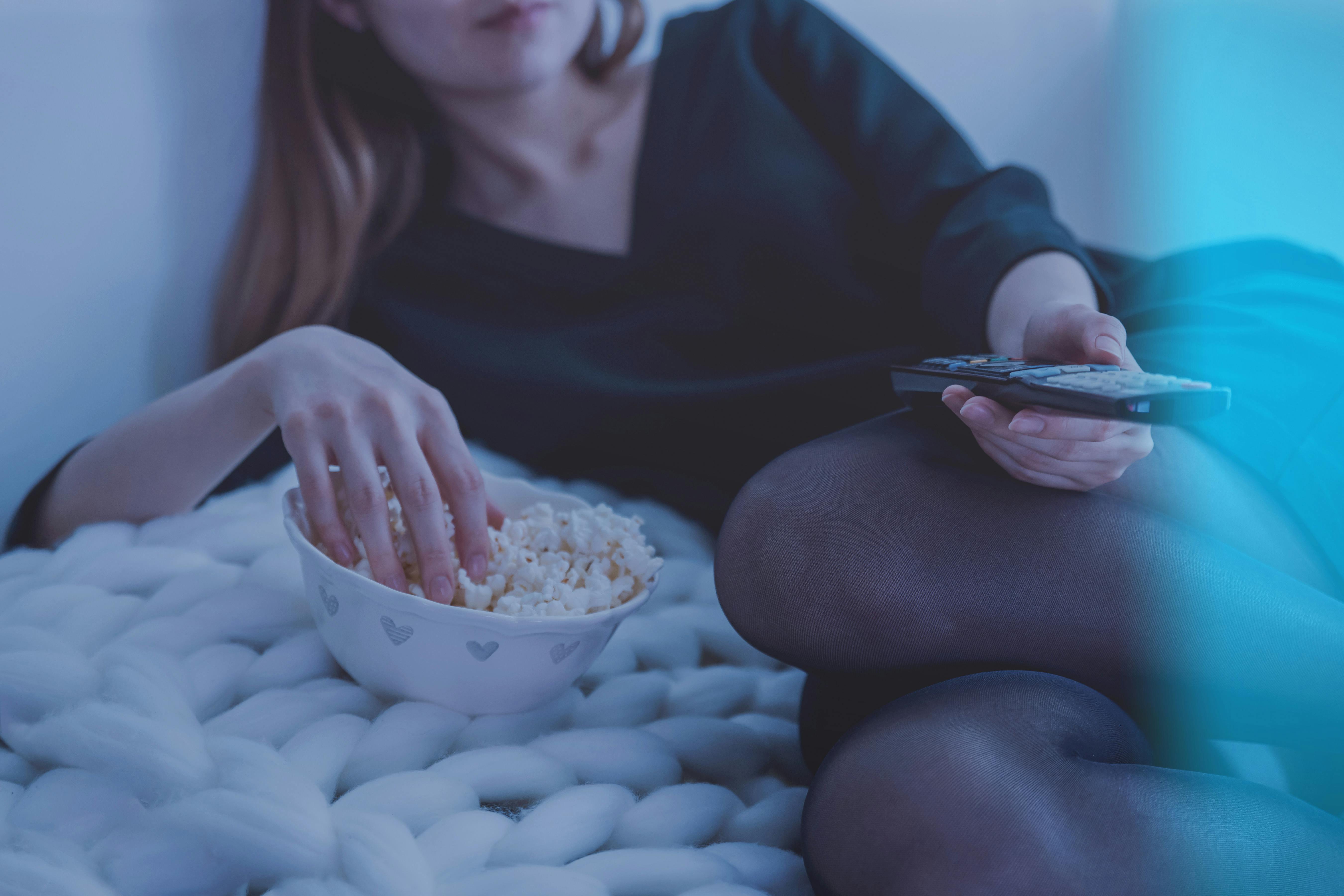 Una mujer comiendo un bol de palomitas y sujetando el mando de la televisión | Fuente: Pexels