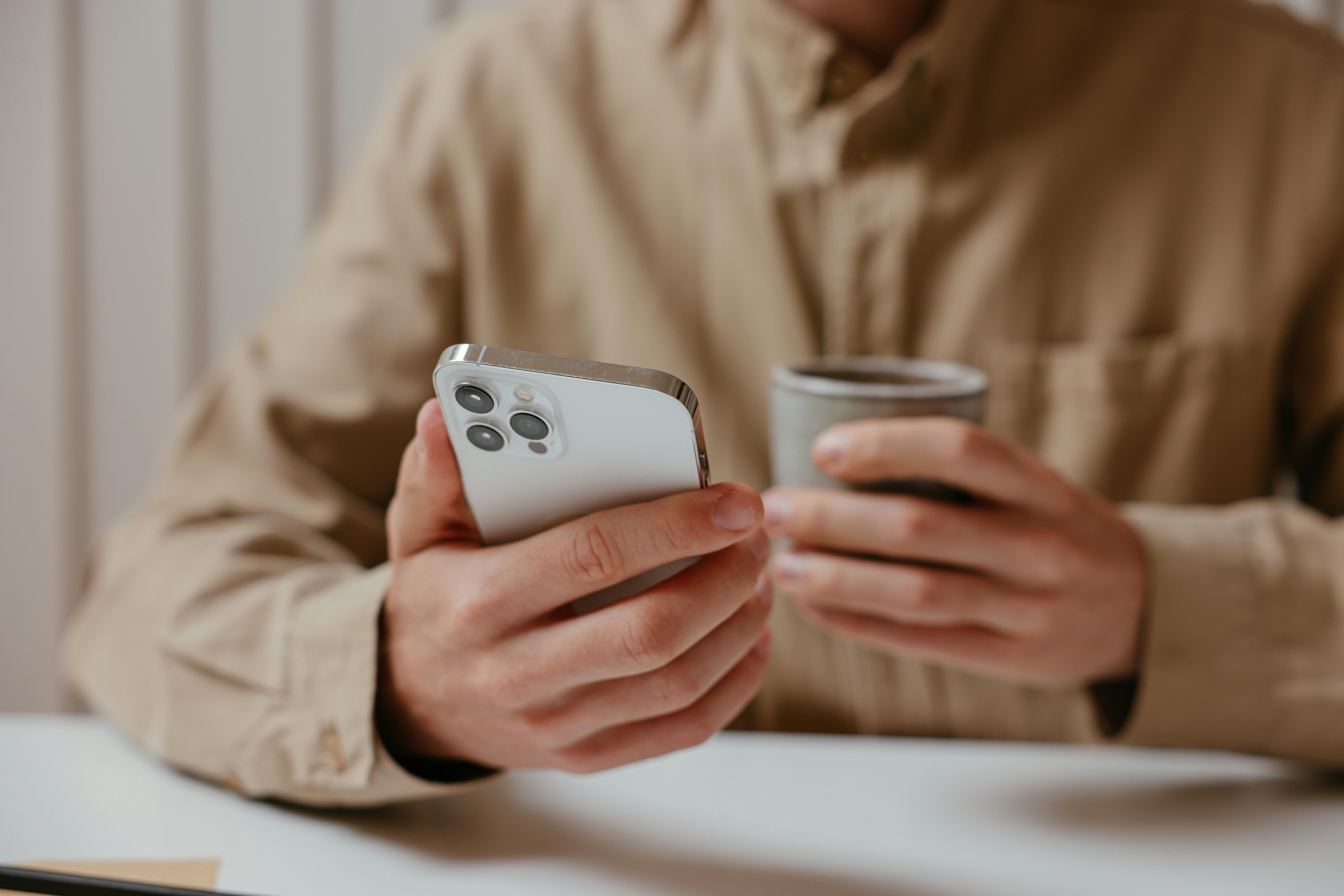 Un hombre con un teléfono y una taza de café en la mano | Fuente: Pexels