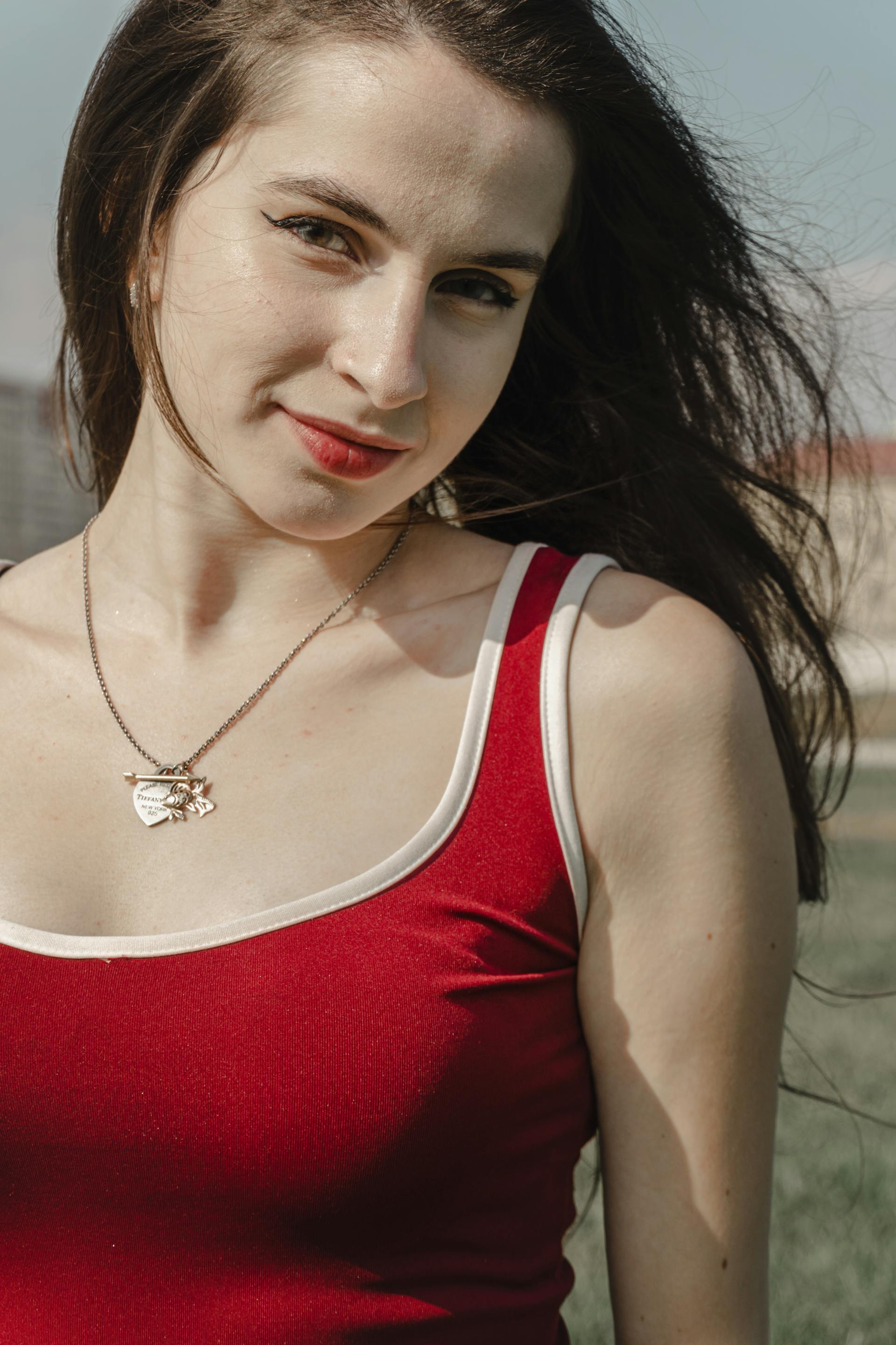 Uma mulher de blusa vermelha sorri enquanto está em pé ao ar livre | Fonte: Pexels