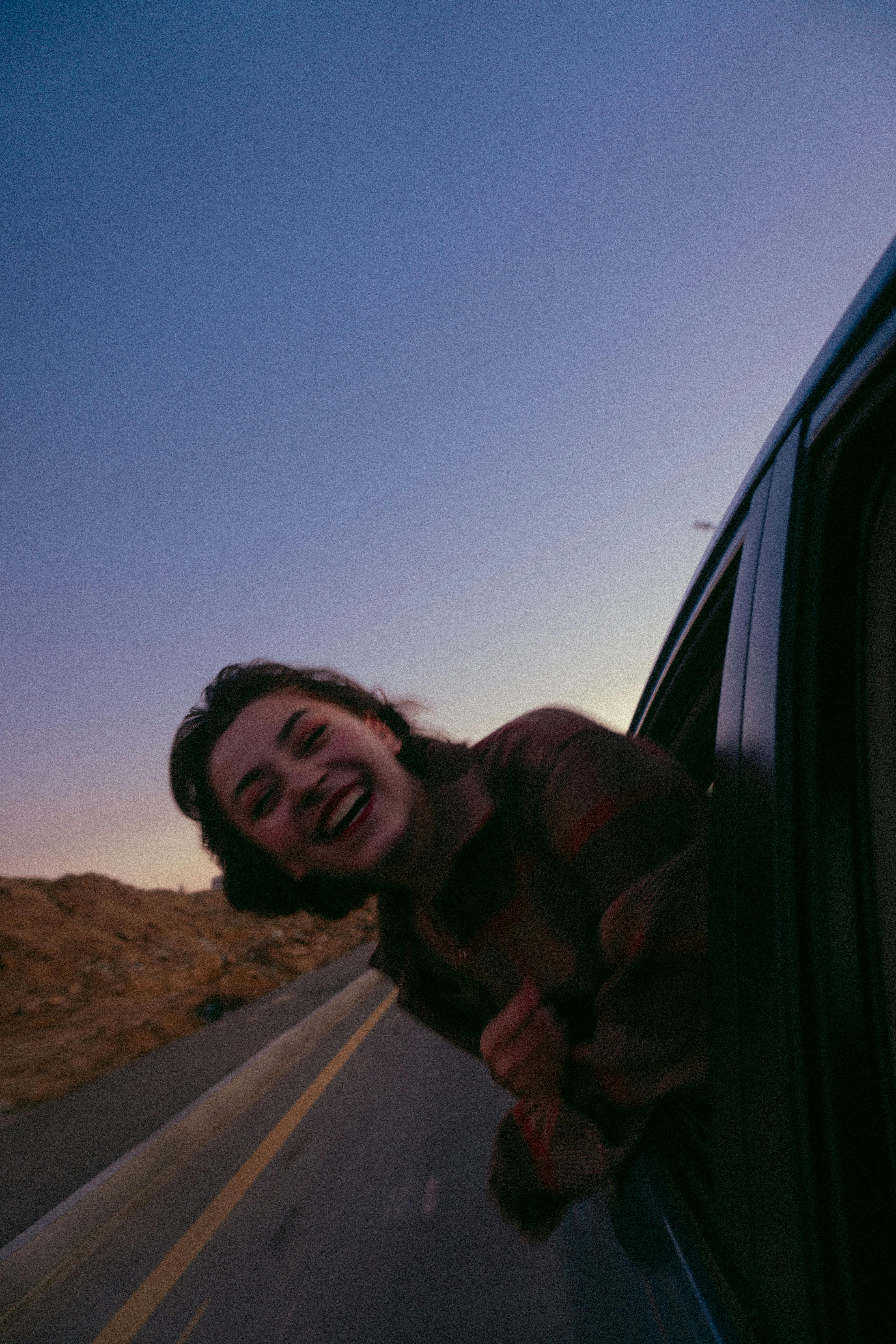 Una adolescente sonriente con la cabeza fuera de la ventanilla de un automóvil | Fuente: Pexels