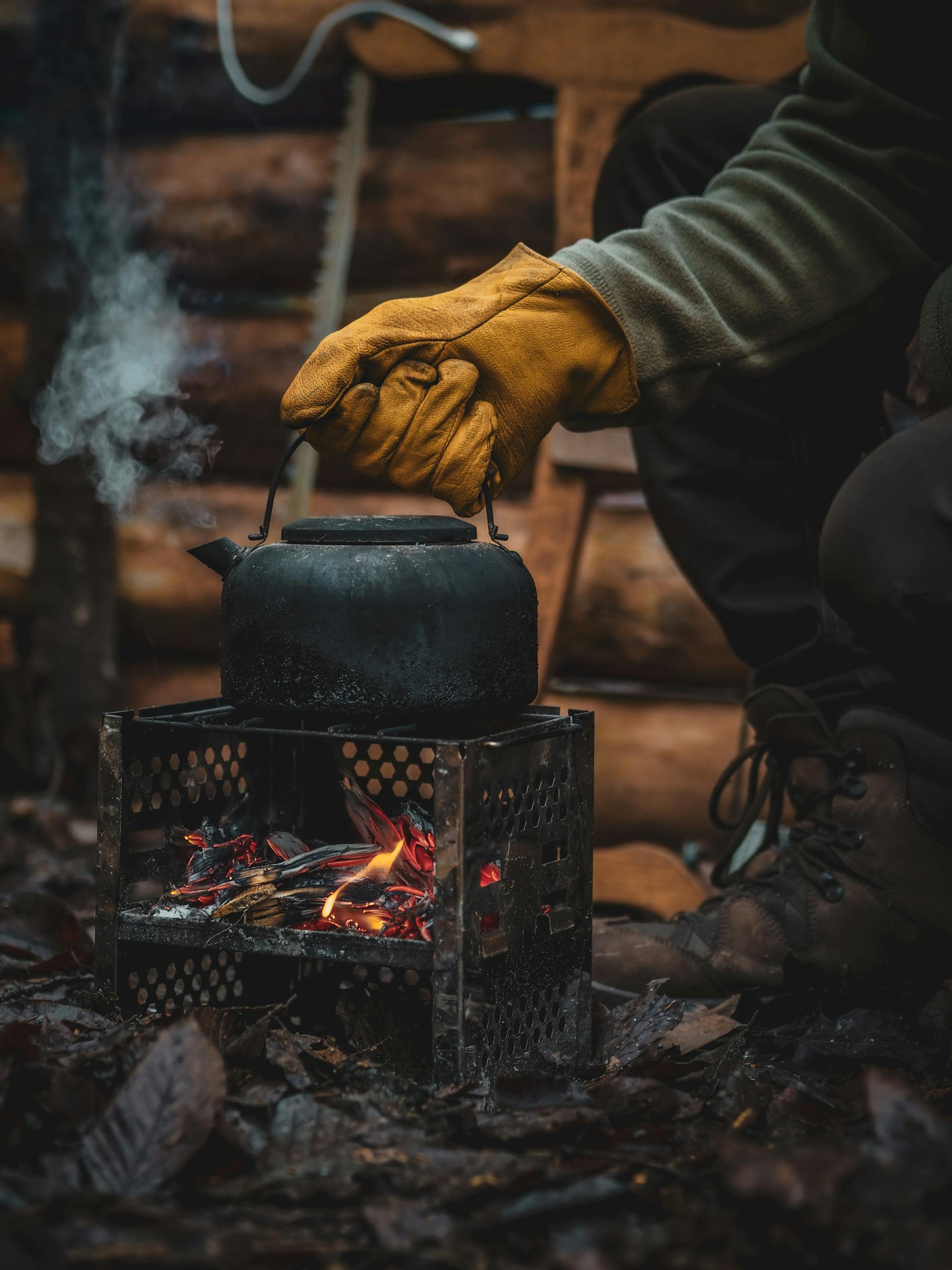Primer plano de una persona que lleva un guante de mano y sostiene una tetera sobre el fuego | Fuente: Pexels