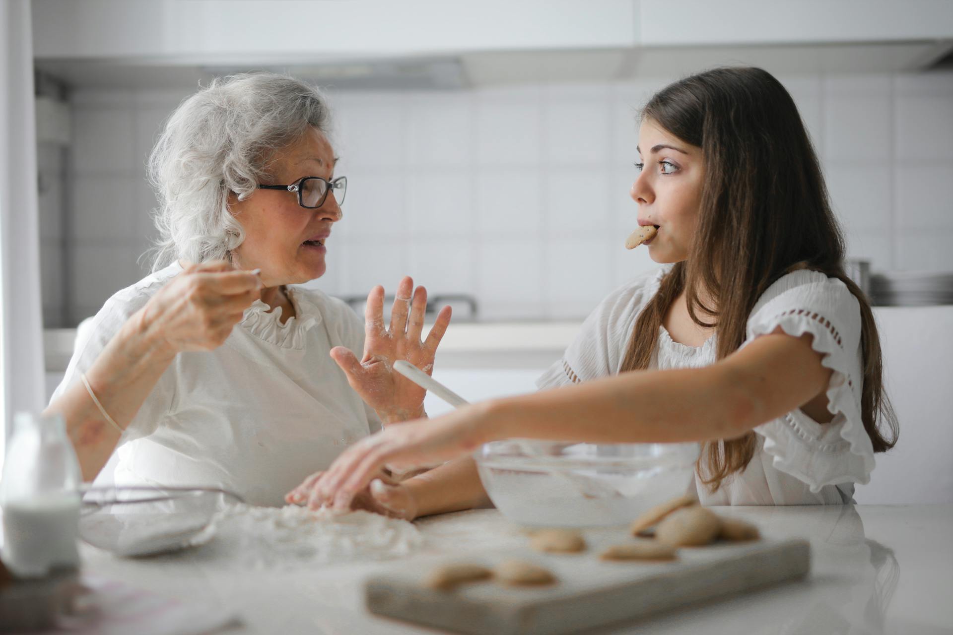 Una mujer mayor horneando con una adolescente que se está comiendo una galleta | Fuente: Pexels