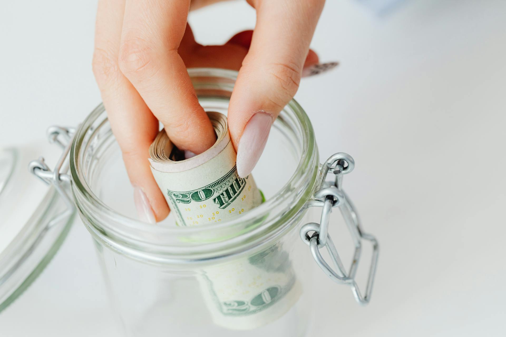Una mujer sacando un rollo de billetes de dólar de un tarro de cristal | Fuente: Pexels