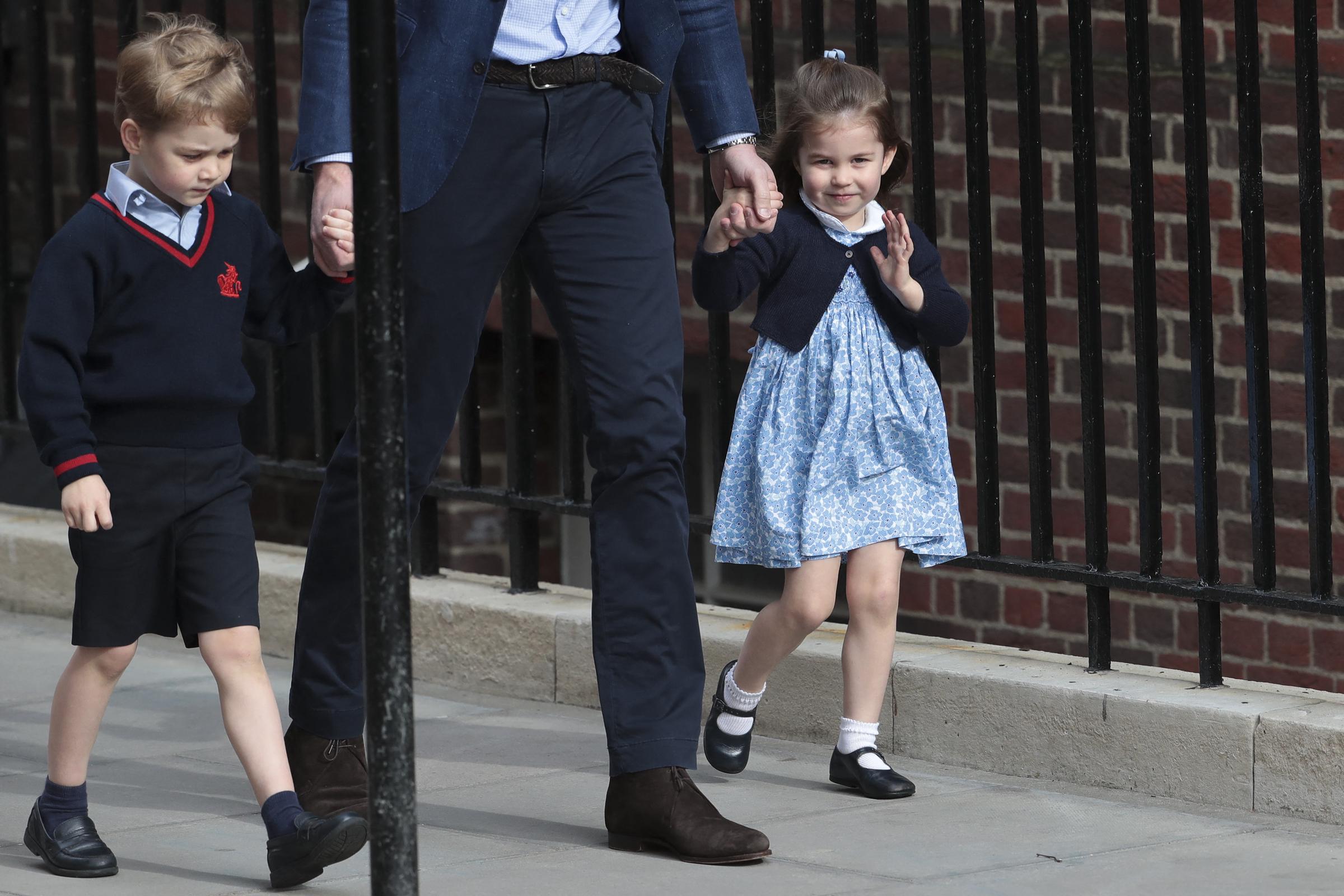 La princesa Charlotte de Cambridge saluda con ternura a los curiosos frente al ala Lindo del Hospital St Mary's el 23 de abril de 2018, en Londres, Inglaterra, al llegar con su padre, el príncipe Guillermo, y su hermano, el príncipe Jorge, para conocer a su hermanito recién nacido. La pequeña de la realeza está encantadora con un vestido tipo smock de flores azules y blancas, combinado con un cárdigan azul marino, calcetines blancos y zapatos tipo Mary Jane, mientras coge de la mano a su padre. | Fuente: Getty Images