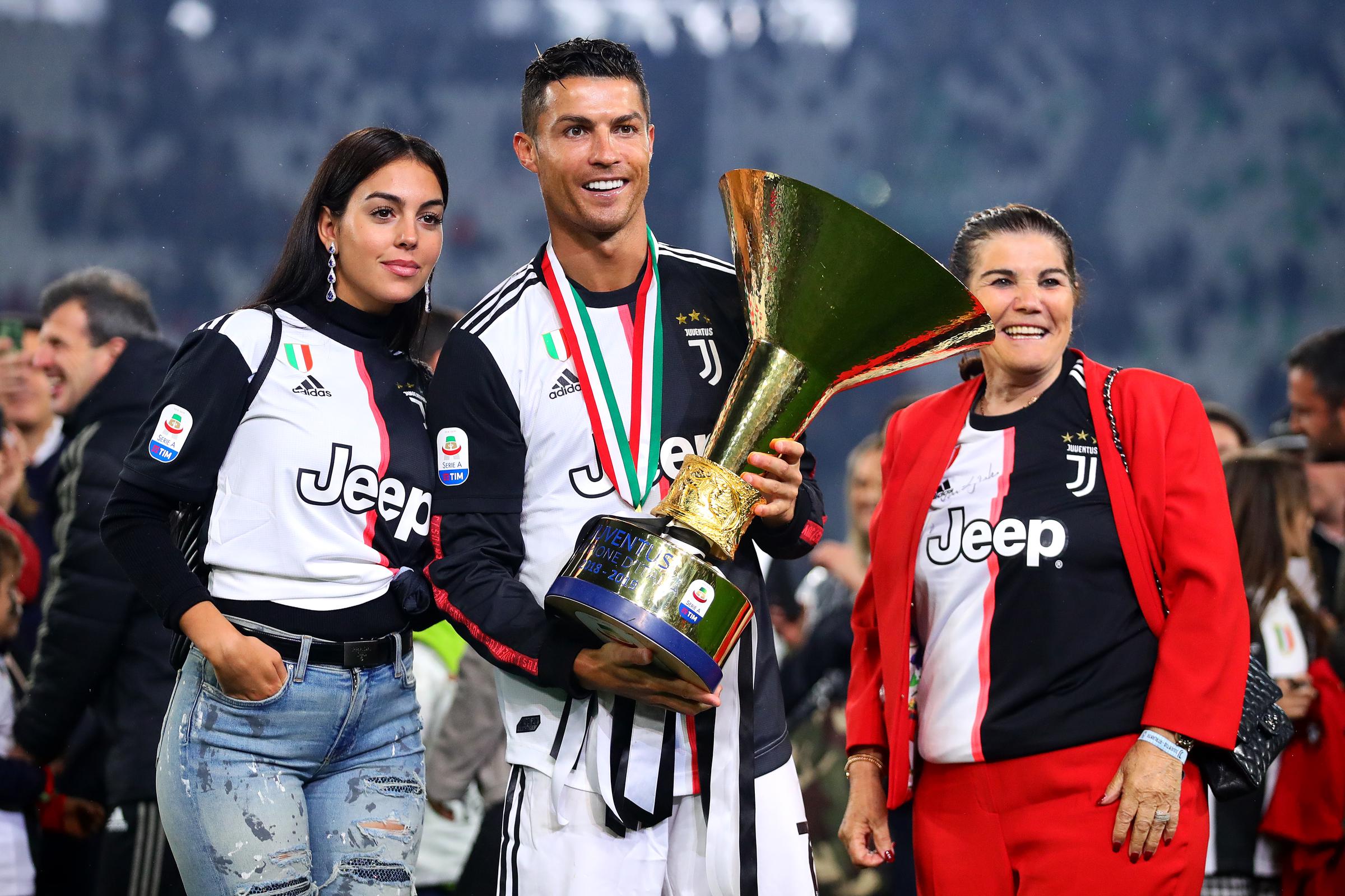 Cristiano Ronaldo, de la Juventus, posa con el trofeo de la Serie A junto a su novia Georgina Rodríguez (izquierda) y su madre Maria Dolores dos Santos Aveiro tras el partido de la Serie A entre la Juventus y el Atalanta BC en el Allianz Stadium el 19 de mayo de 2019 en Turín, Italia. | Fuente: Getty Images.