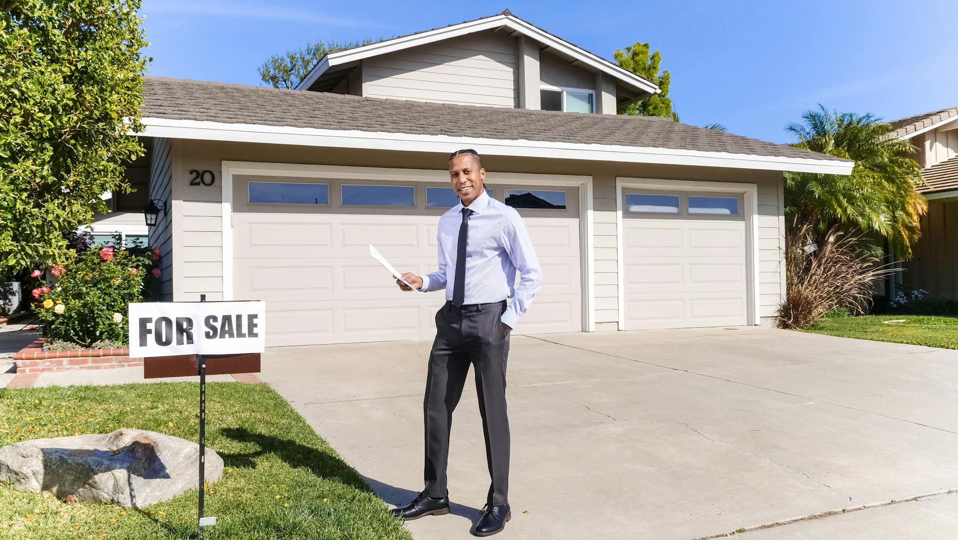 Un hombre sonriente delante de una casa con un cartel de se vende | Fuente: Pexels