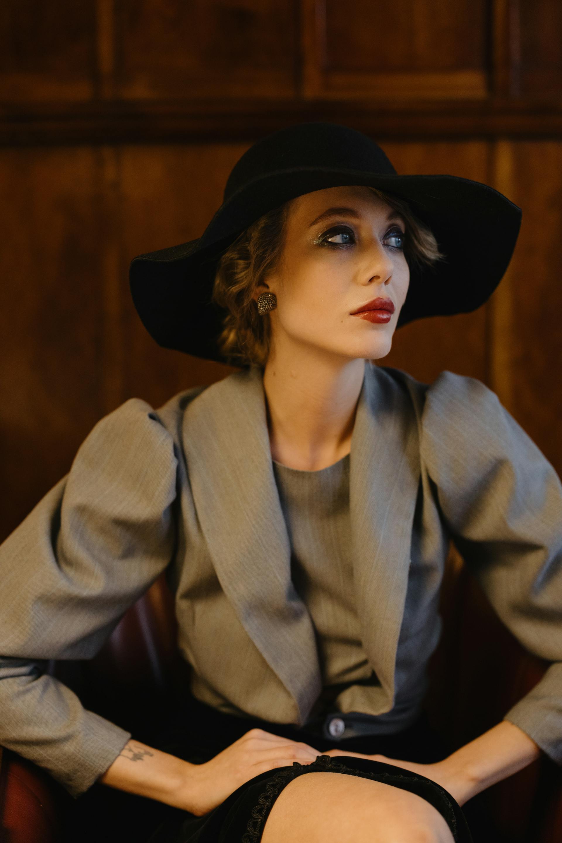 Una mujer a la moda con los labios pintados de rojo y un sombrero negro mirando a un lado | Fuente: Pexels