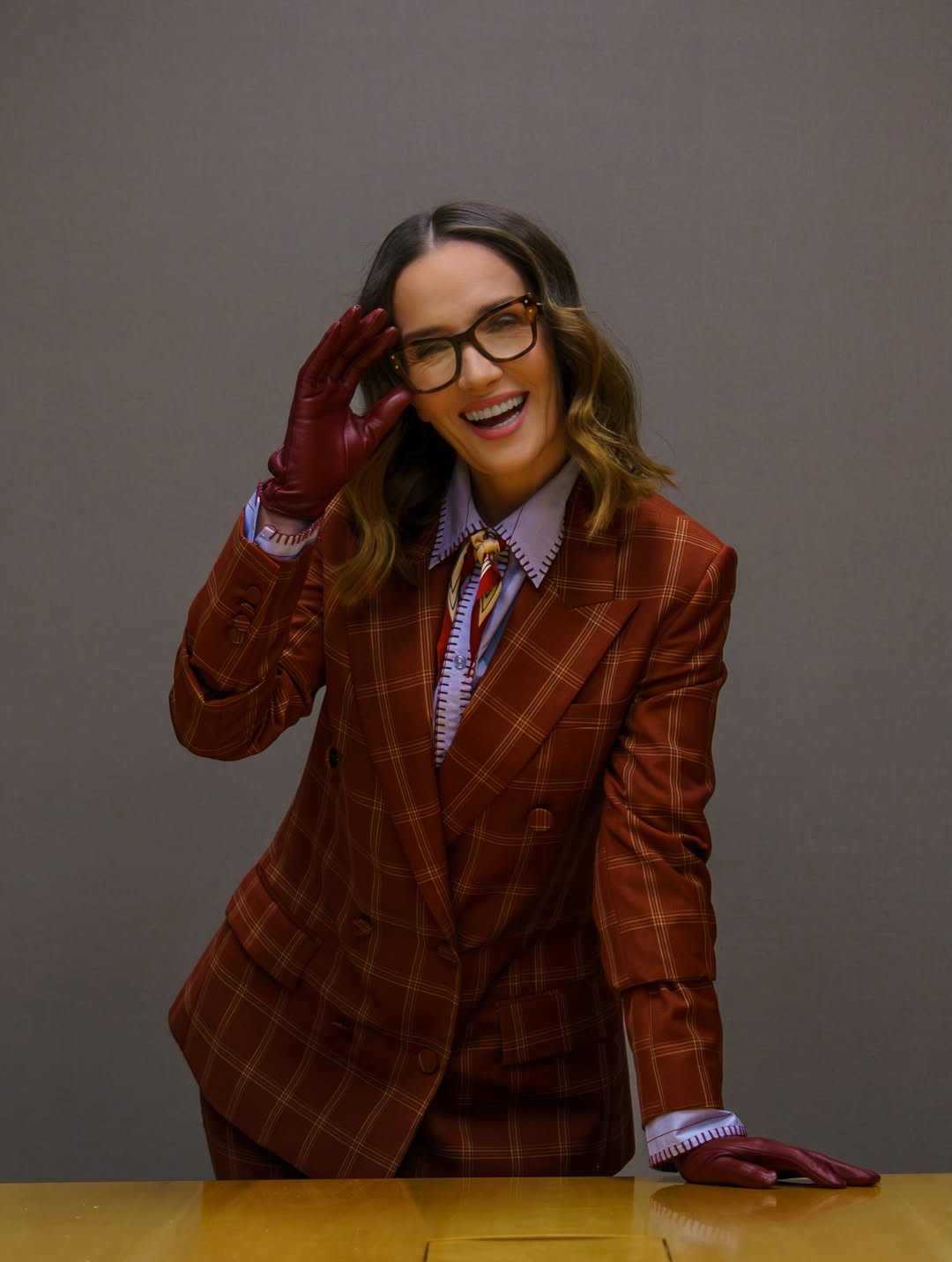 Natalia Oreiro sonríe mientras posa con gafas de armazón oscuro y guantes burdeos durante una actividad promocional de “Nada entre los dos”. | Fuente: Instagram/nataliaoreirosoy