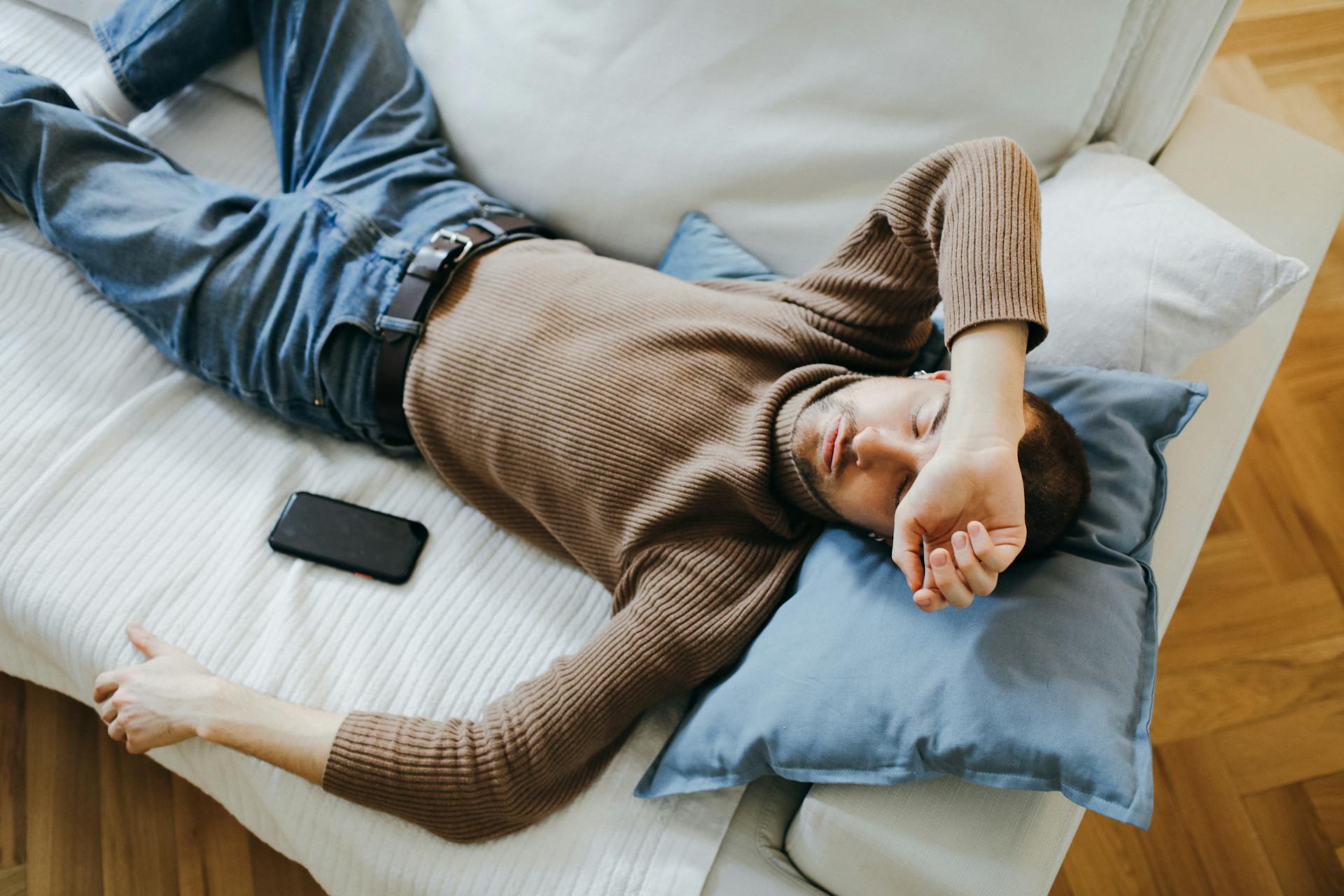 Un hombre durmiendo en el sofá con su teléfono al lado | Fuente: Pexels