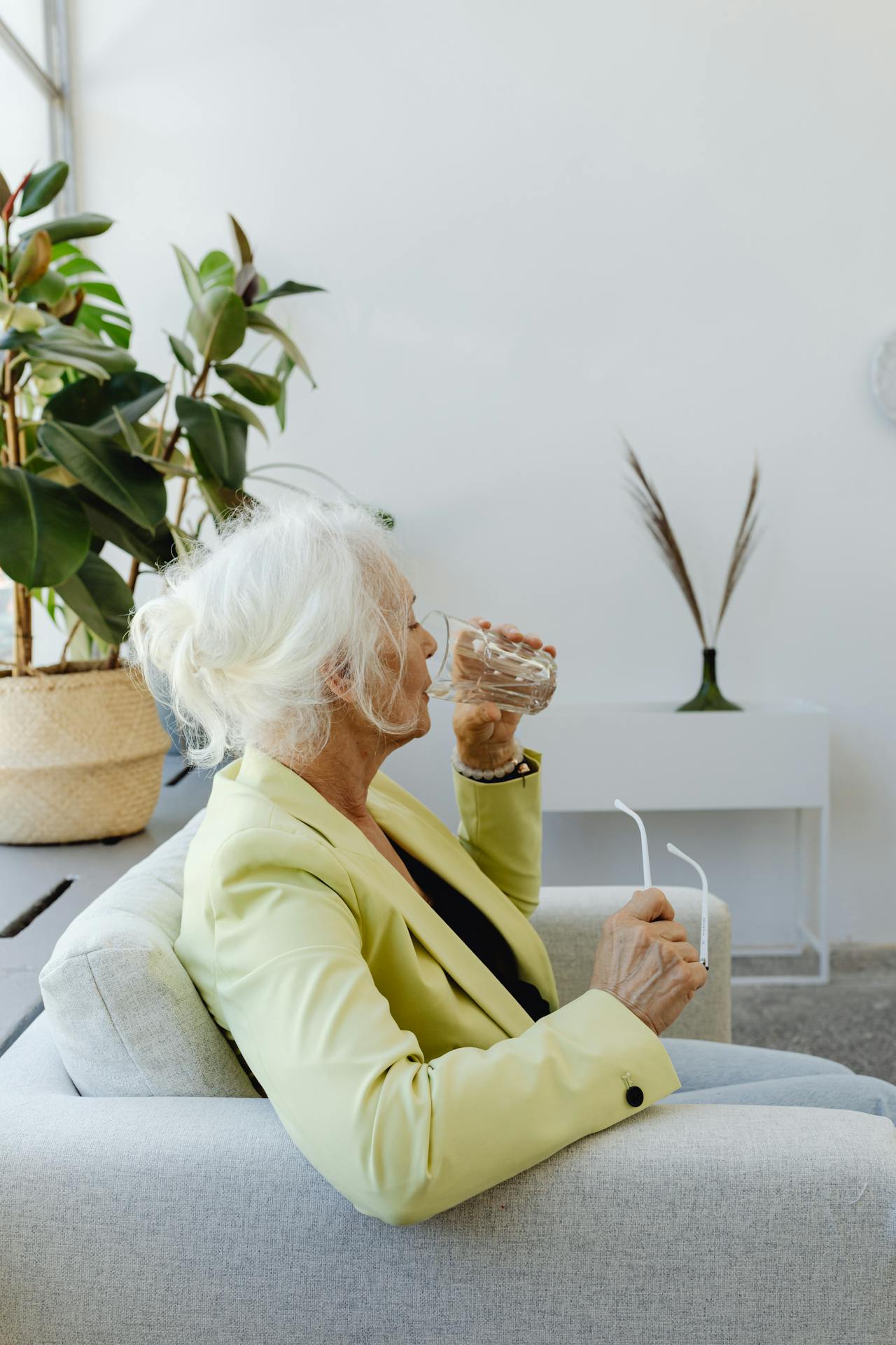 Una mujer mayor sentada en el sofá y bebiendo un vaso de agua | Fuente: Pexels