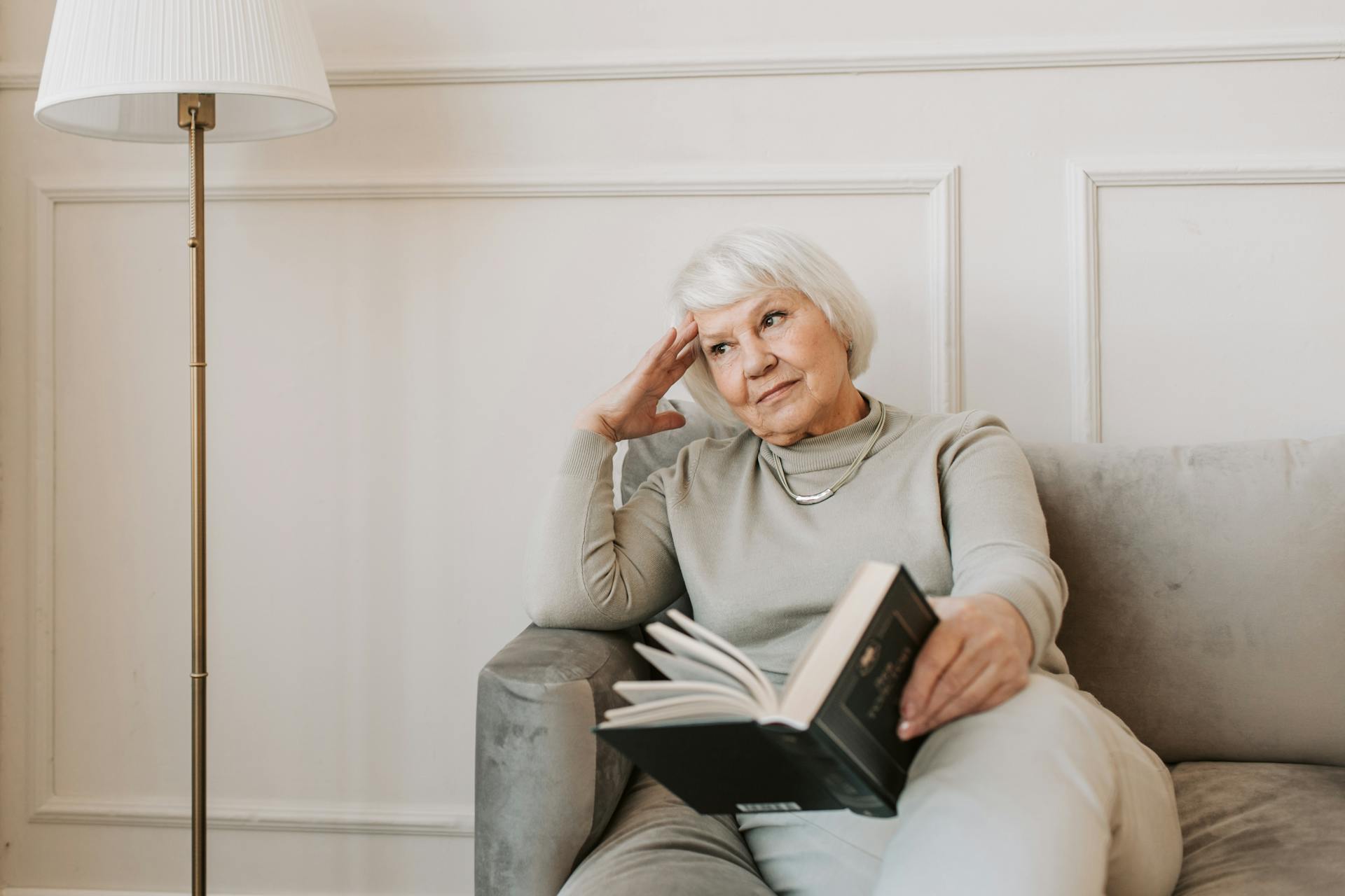 Una anciana pensativa sentada en un sofá con un libro | Fuente: Pexels