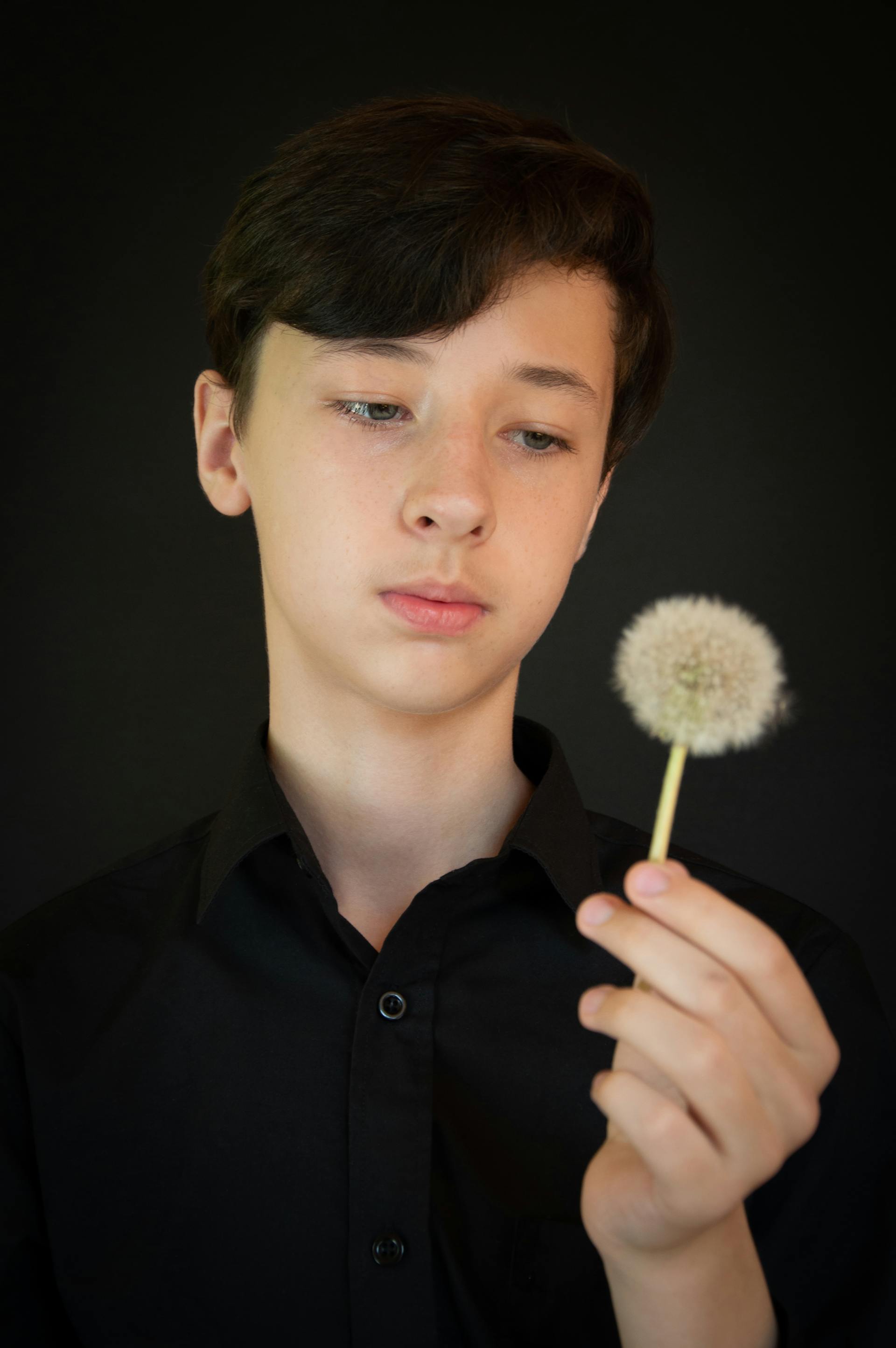 Un adolescente mirando un diente de león en la mano | Fuente: Pexels