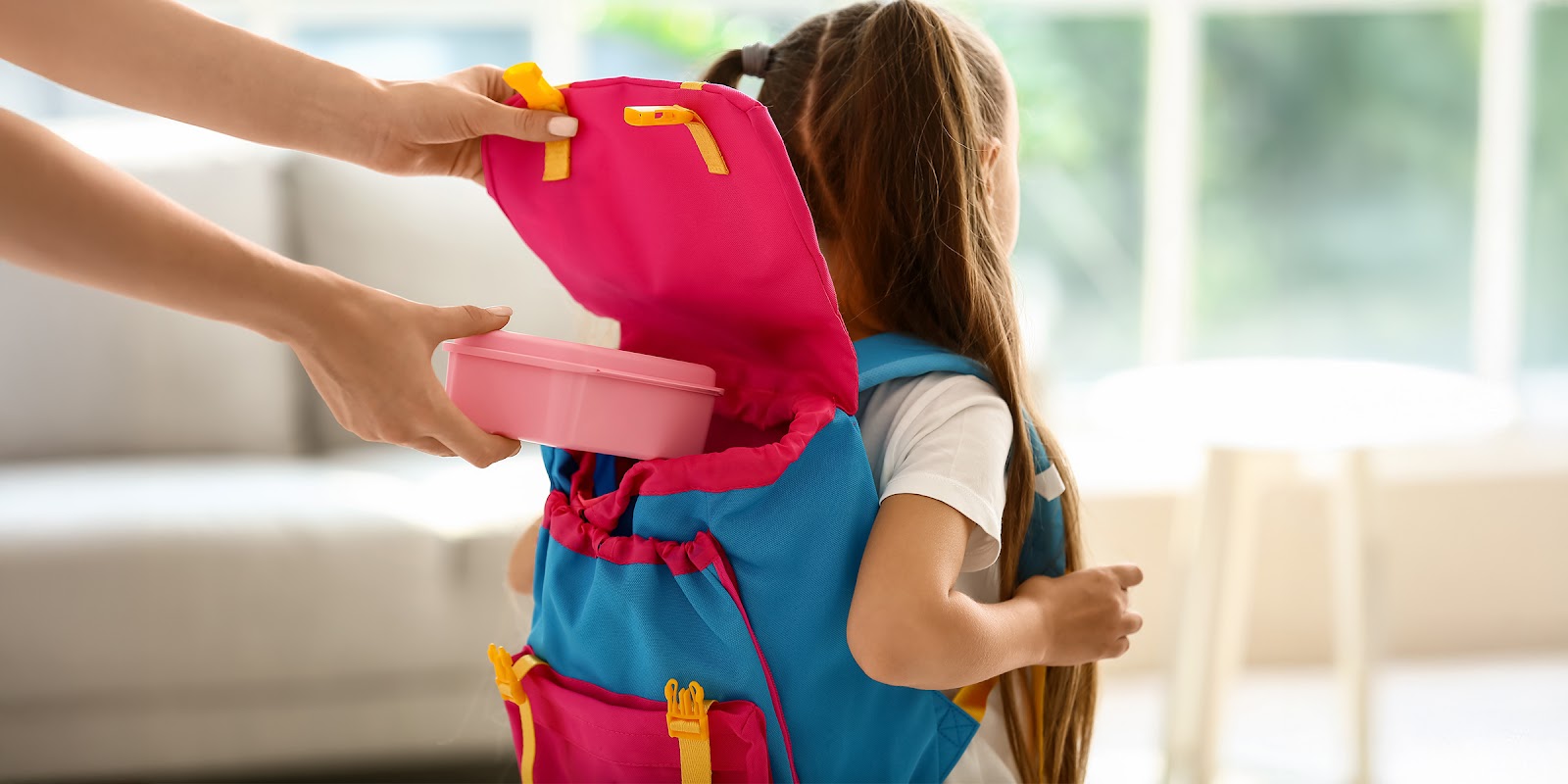 Un adulto colocando una lonchera en la mochila de un niño | Fuente: Shutterstock