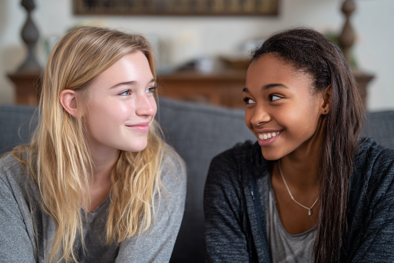 Dos chicas adolescentes sonriéndose en un sofá | Fuente: Midjourney