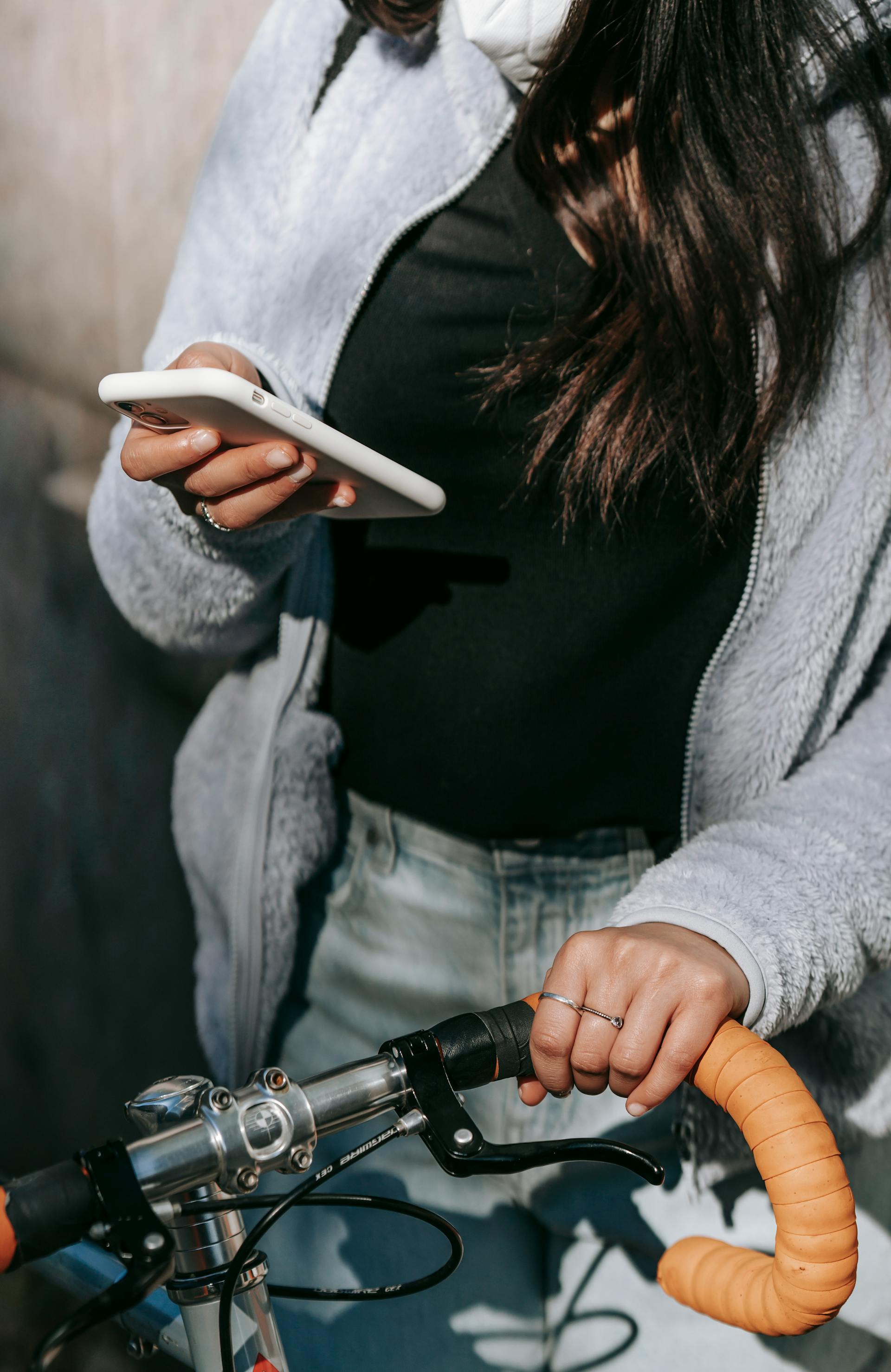 Una joven utilizando su teléfono mientras sujeta el manillar de su bicicleta | Fuente: Pexels
