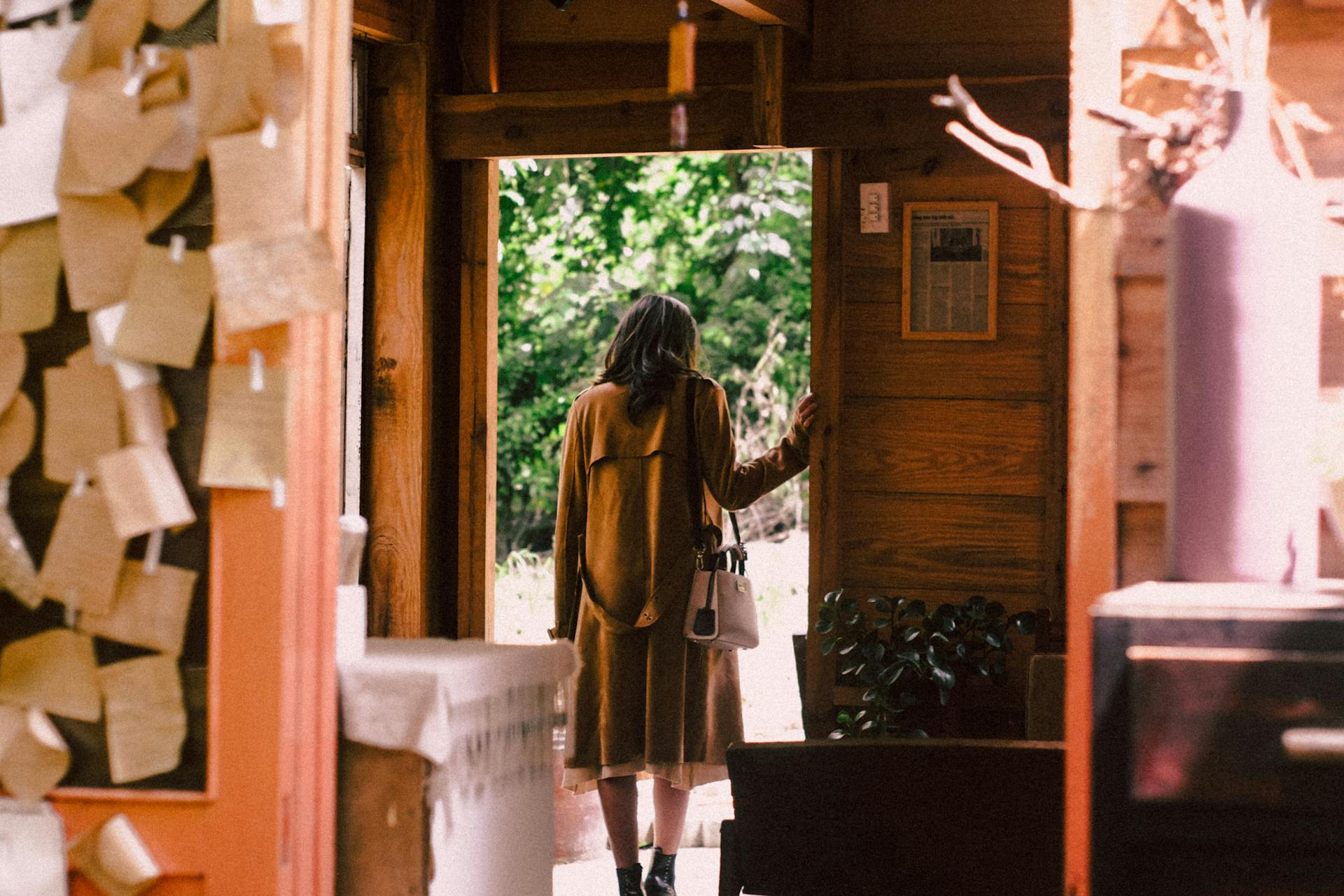 Una mujer con un largo abrigo marrón y botas saliendo de una casa | Fuente: Pexels