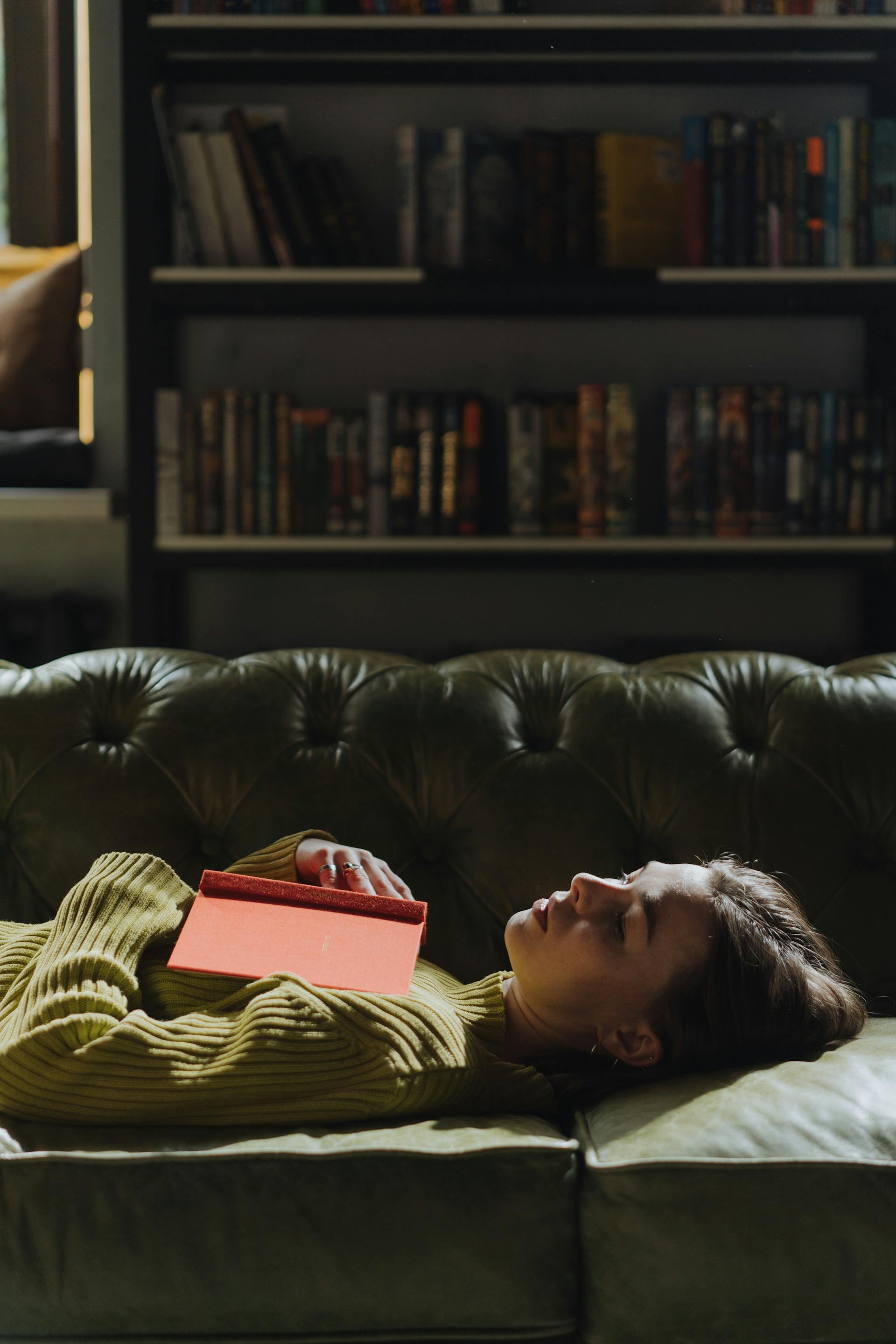 Una mujer tumbada en un sofá con un libro | Fuente: Pexels