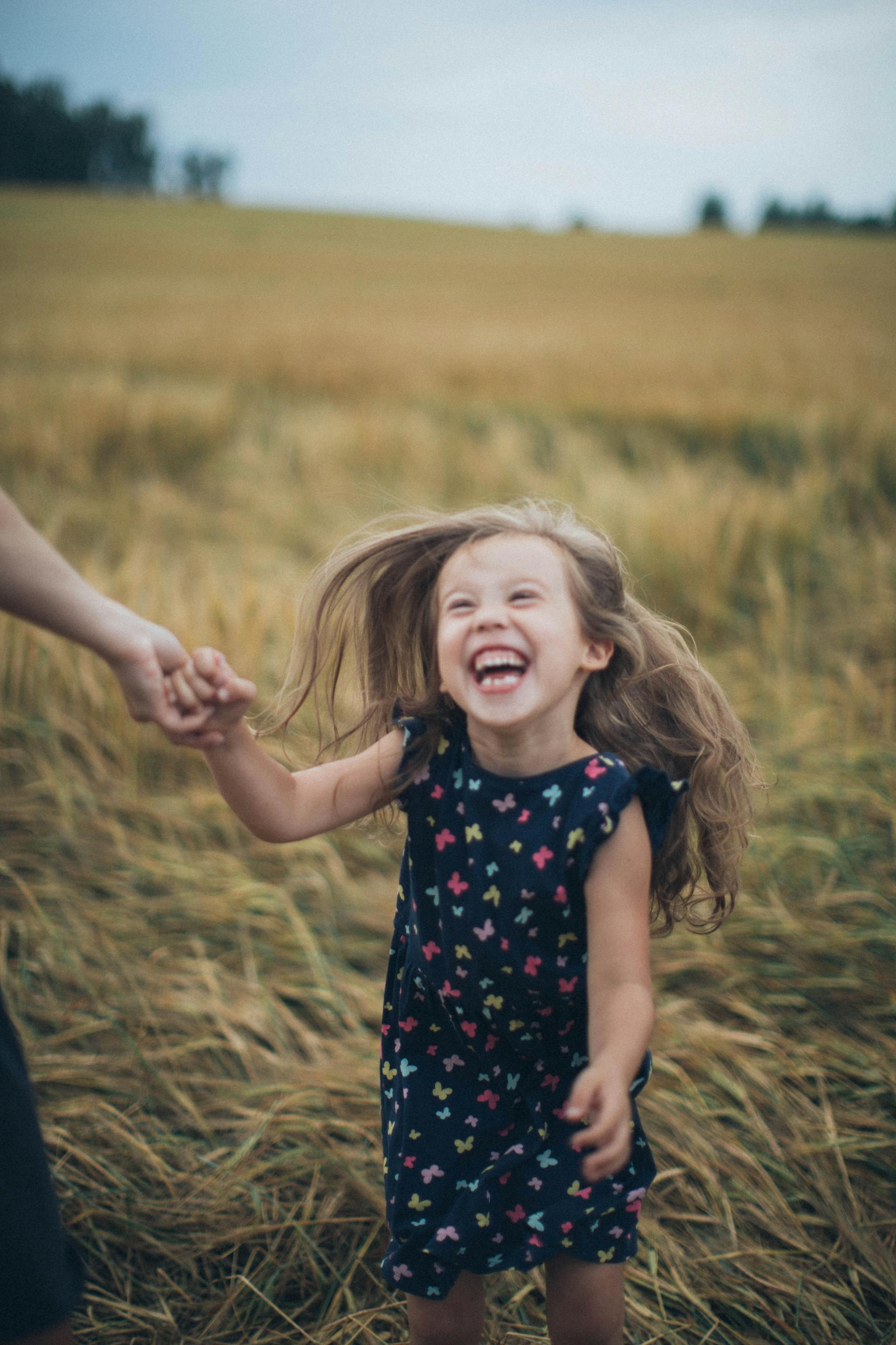 Una niña sonriente cogida de la mano de su madre en un campo | Fuente: Pexels