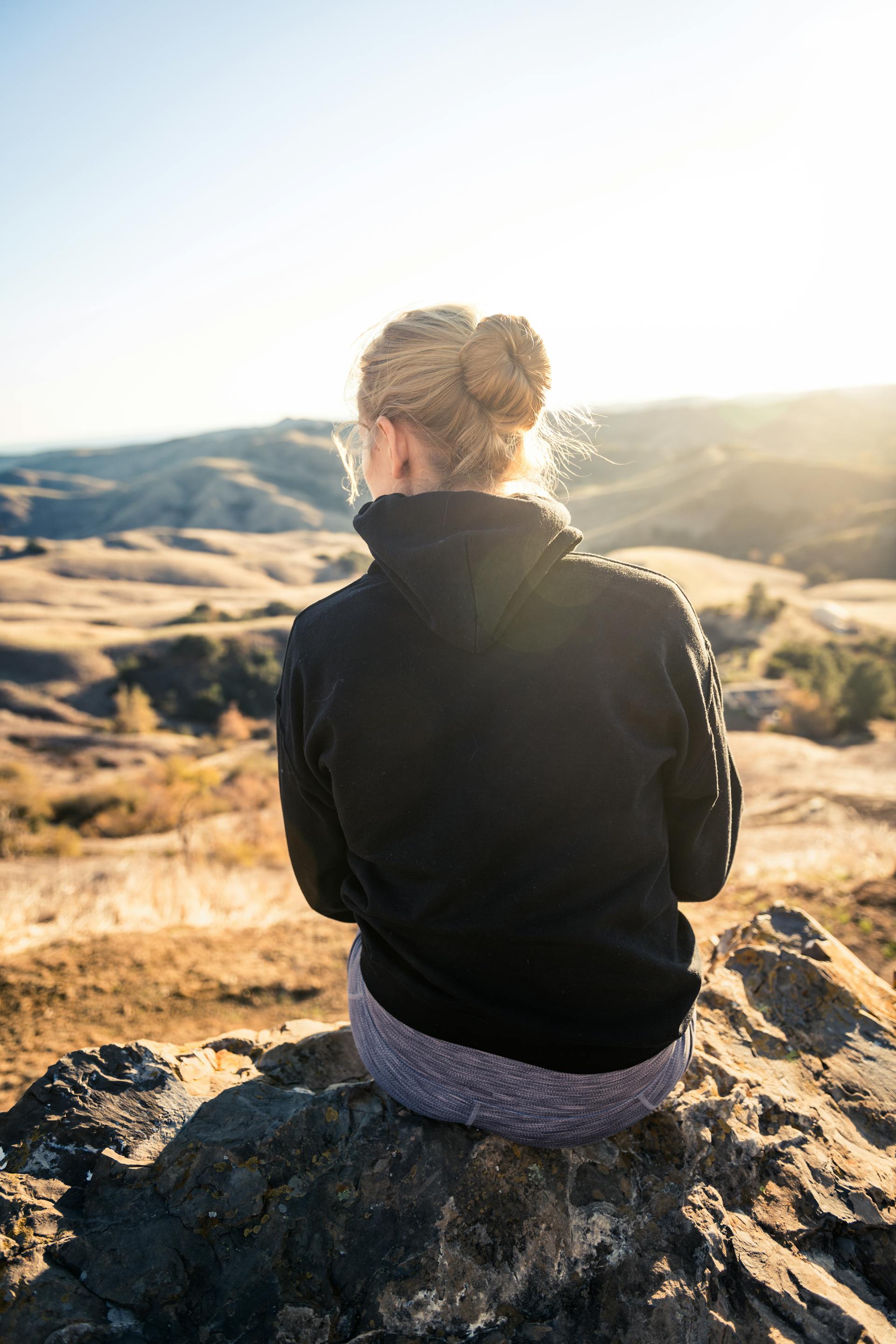 Mujer con sudadera negra sentada en una roca | Fuente: Pexels