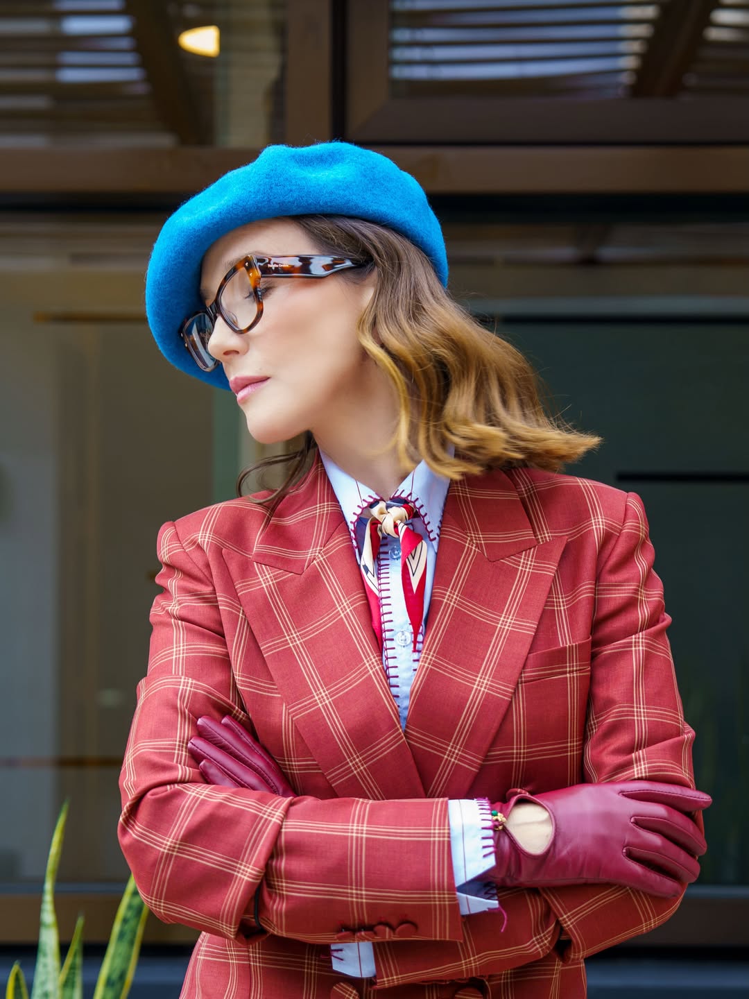 Primer plano de Natalia Oreiro con su look sastrero de cuadros rojizos. La actriz lleva boina azul, gafas de marco carey, guantes burdeos y un pañuelo estampado anudado al cuello, mientras posa con los brazos cruzados. | Fuente: Instagram/nataliaoreirosoy